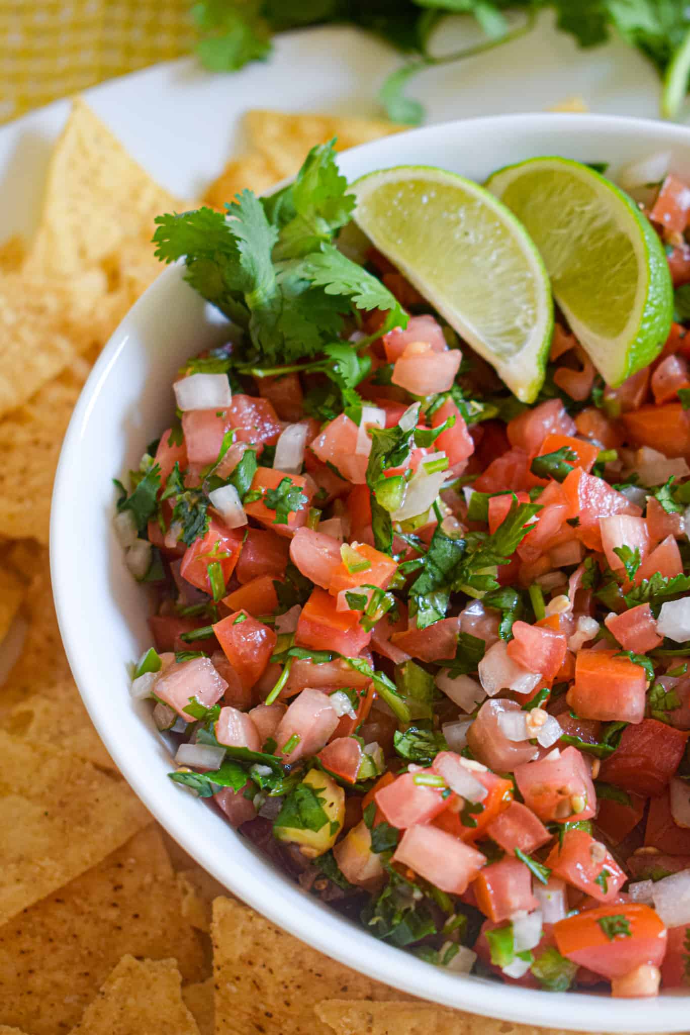 A bowl of Fresh Pico de Gallo garnished with cilantro and lime wedges sits surrounded by crispy tortilla chips.