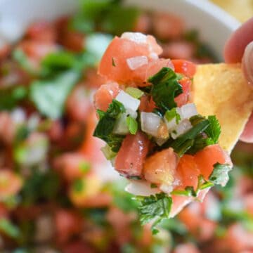 A close-up of a tortilla chip topped with Fresh Pico de Gallo, featuring chopped tomatoes, onions, cilantro, and peppers.