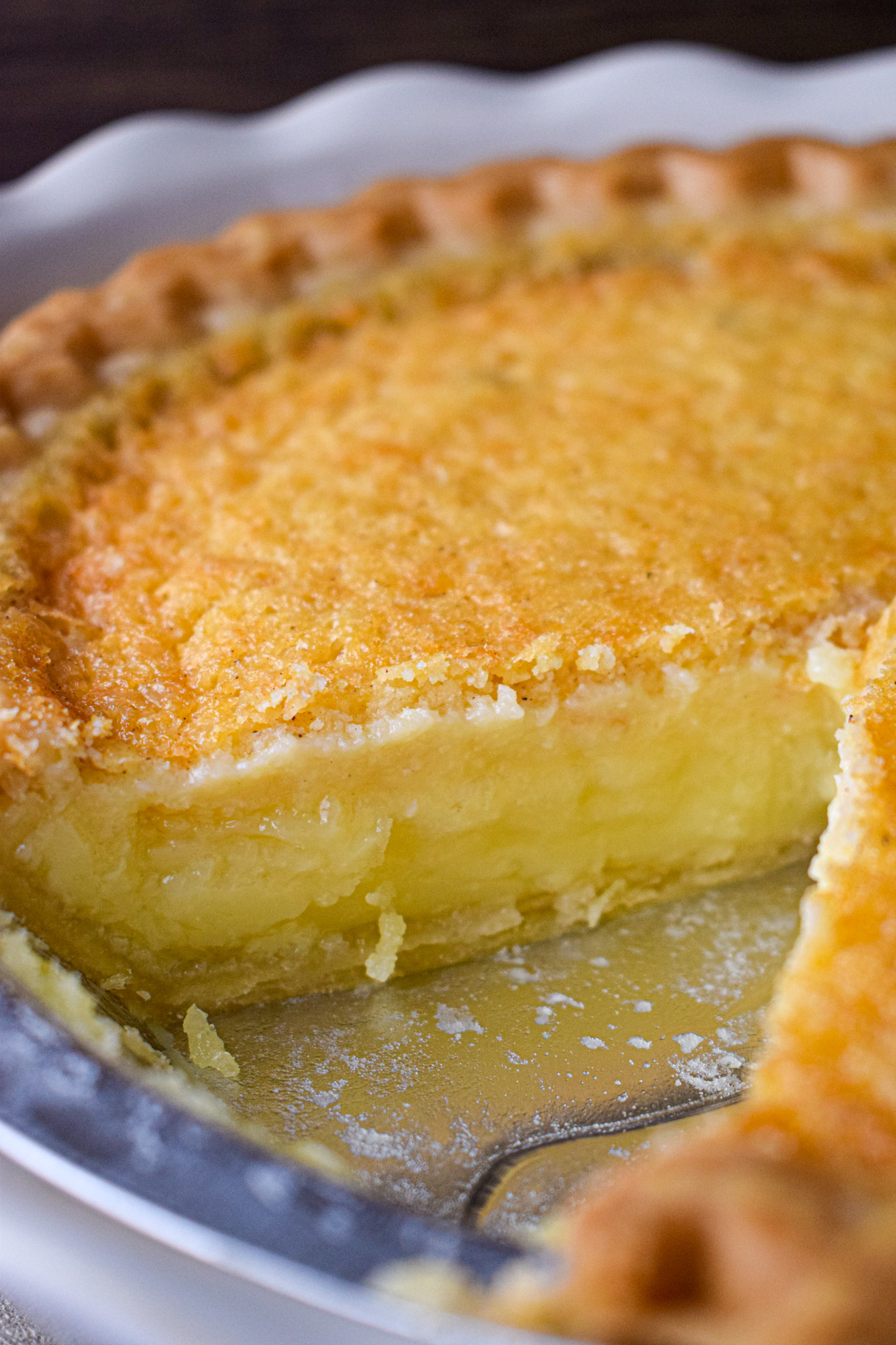 Close-up of a buttermilk pie in a white pie dish with a slice removed, showing the creamy custard filling and golden flaky crust.