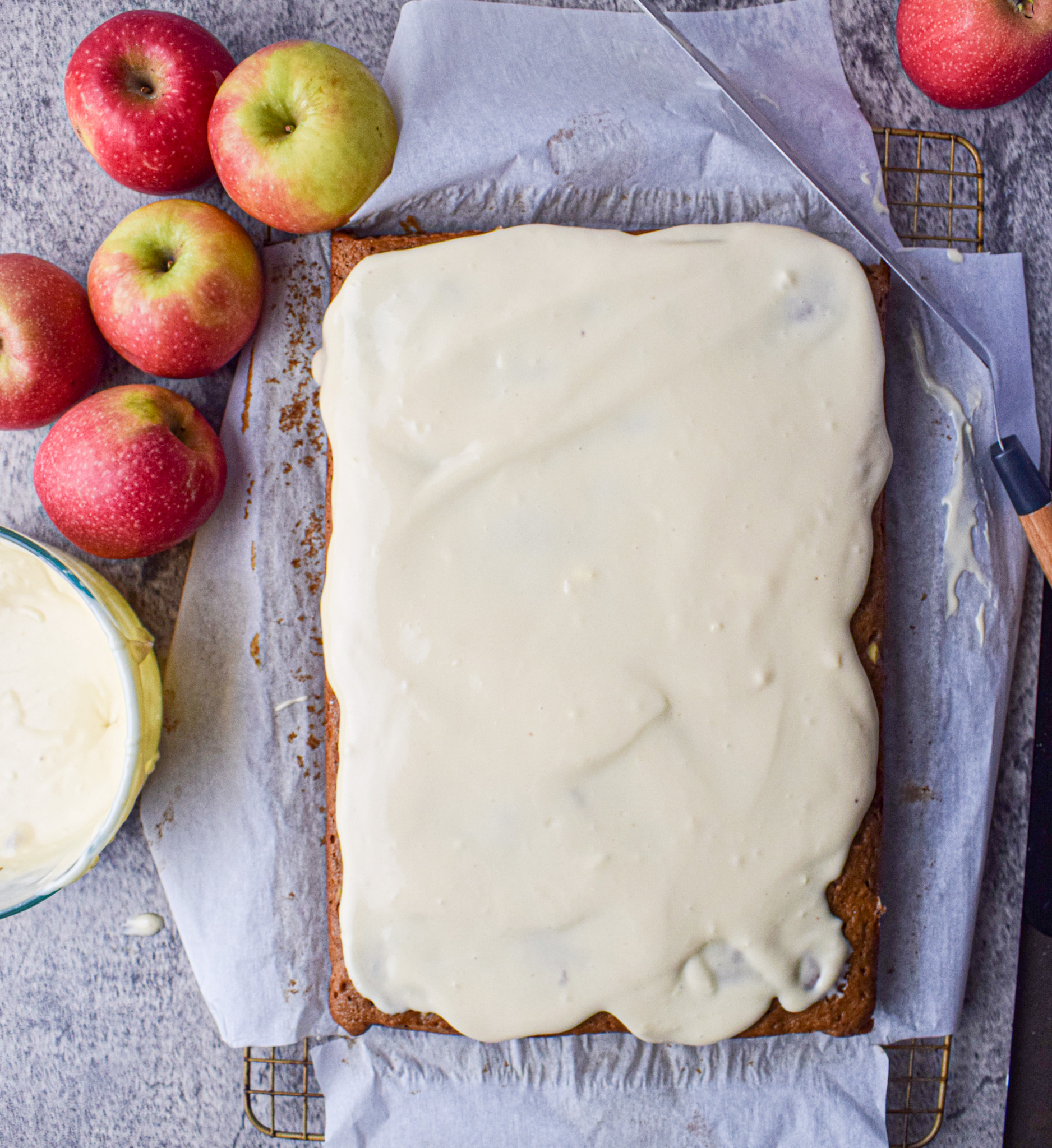 applesauce spice sheet cake with cream cheese frosting on a wire rack surrounded by apples 
