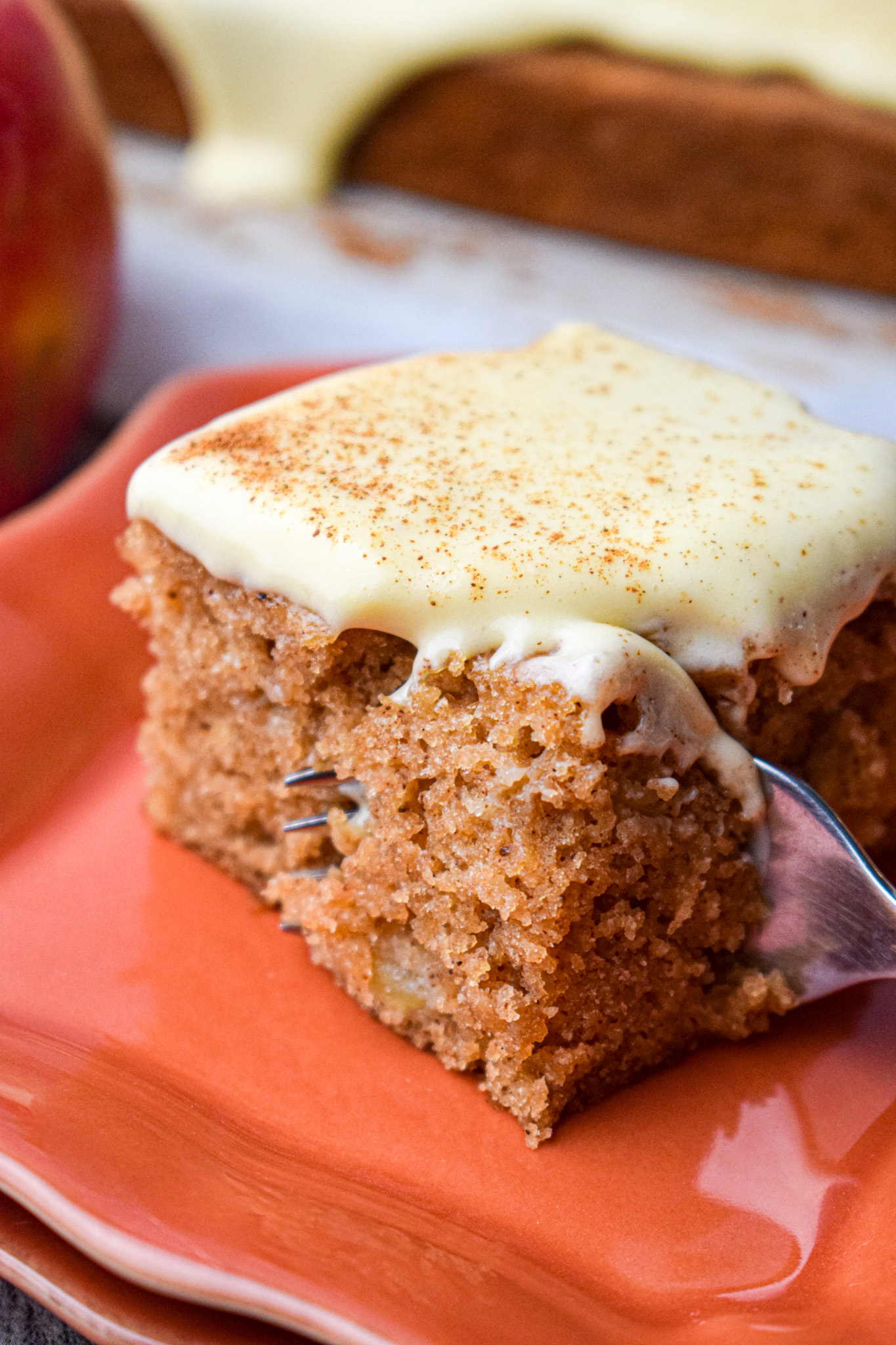 slice of applesauce spice cake with cream cheese frosting and a fork taking a piece