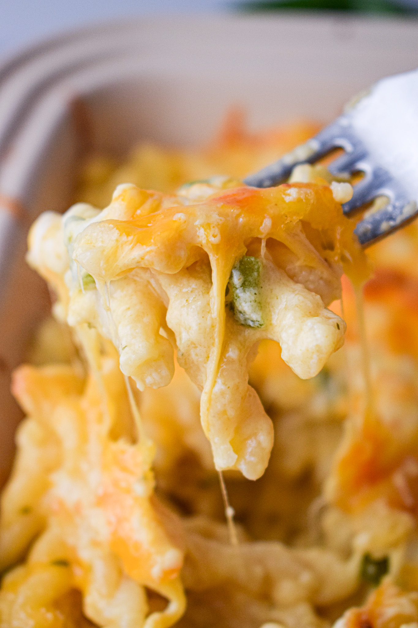 a fork full of mac and cheese with green chiles and a cheese pull