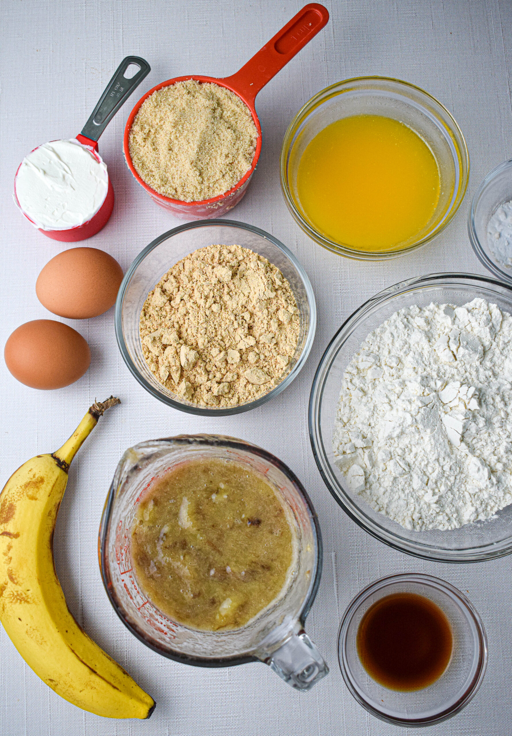 ingredients for banana peanut butter quick bread: flour, mashed bananas, eggs, peanut butter powder, brown sugar, sour cream. melted butter, vanilla extract, baking soda