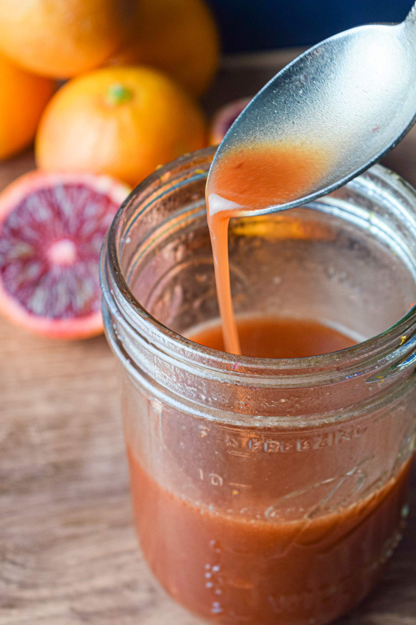 spoon pouring blood orange dressing into a mason jar