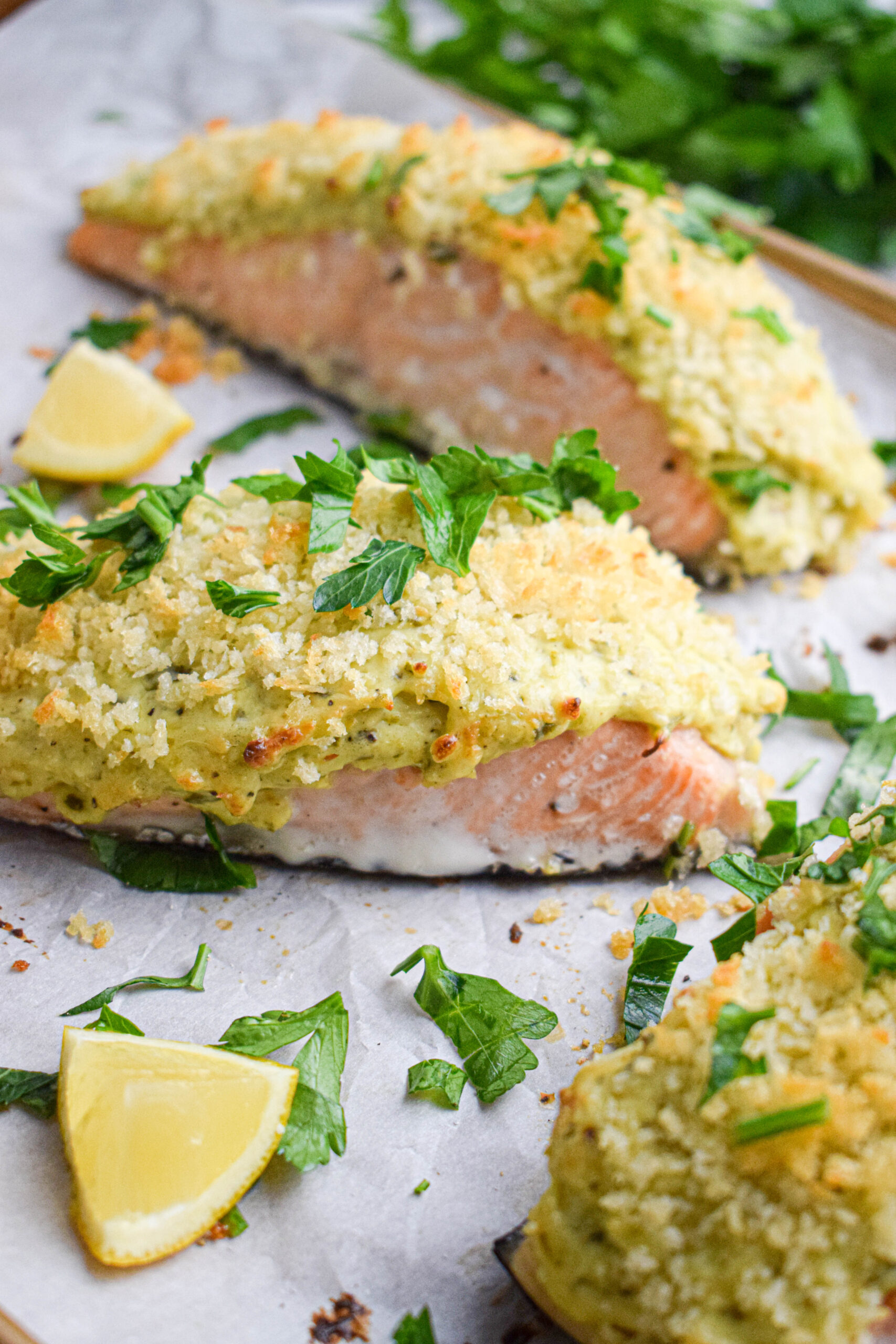 pesto crusted salmon topped with panko bread crumbs and parsley next to a lemon wedge