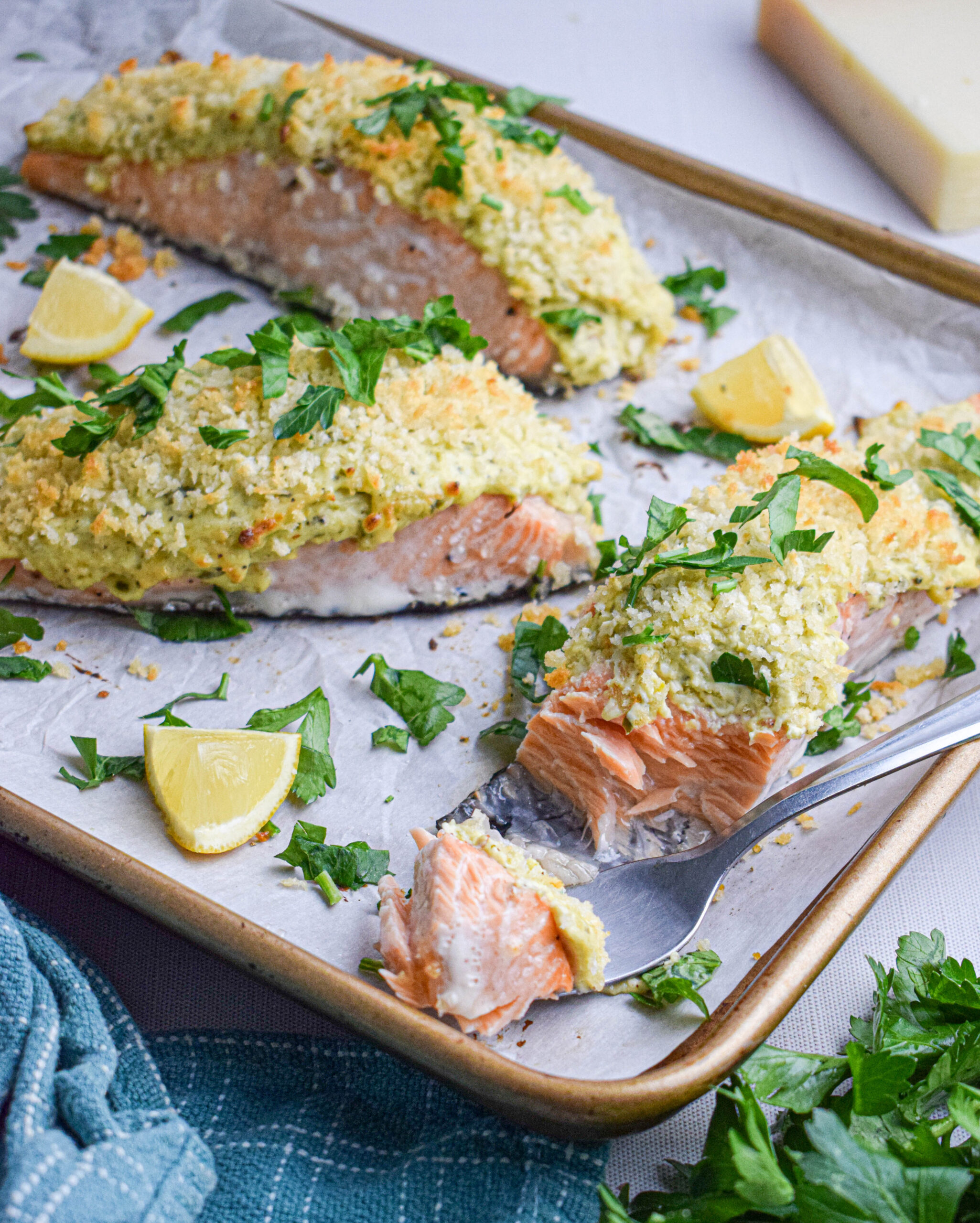 fork flaking pesto crusted salmon on a parchment lined baking sheet 