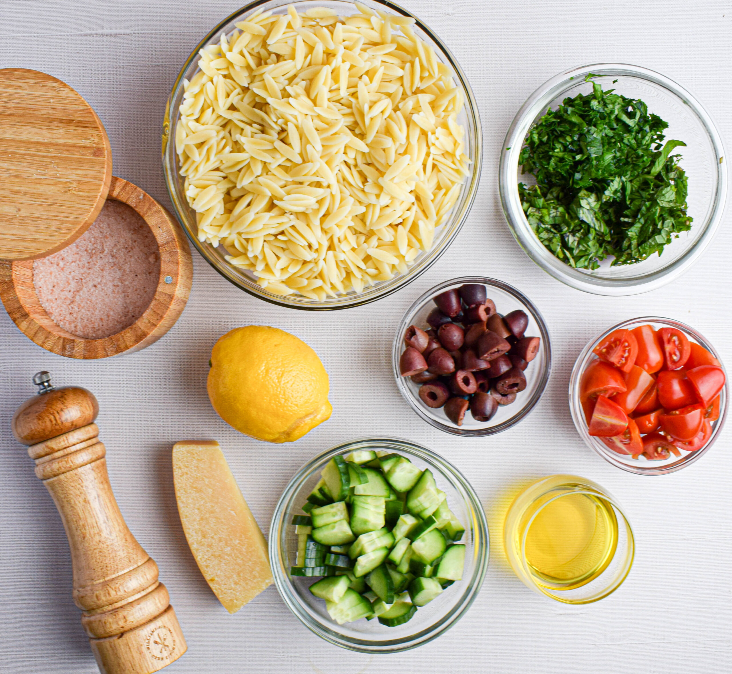 ingredients for lemon orzo salad: orzo, kalamata olives, basil, mint, parsley, cherry tomatoes, cucumber, olive oil, lemon, salt and pepper