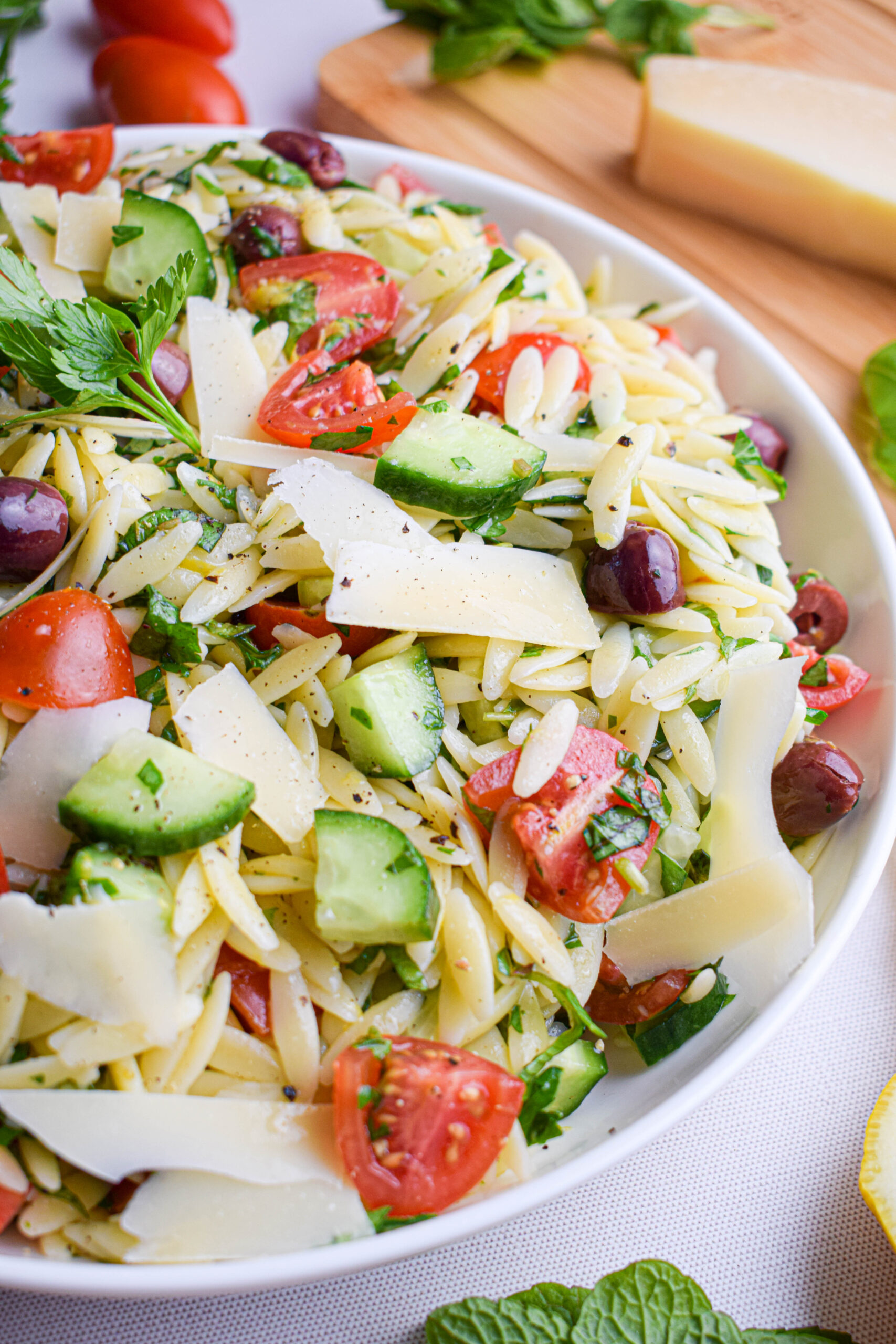 bowl of spring and summer recipe for lemon orzo pasta salad with cucumbers, tomatoes, olives and parmesan shavings 