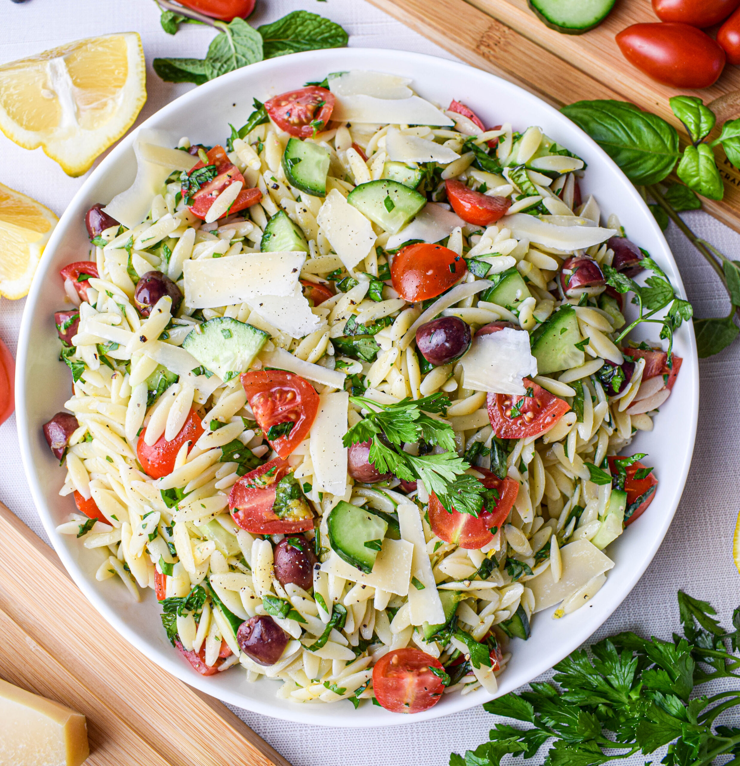bowl filled with lemon orzo pasta salad with cucumbers, tomatoes, olives, parmesan cheese and fresh herbs