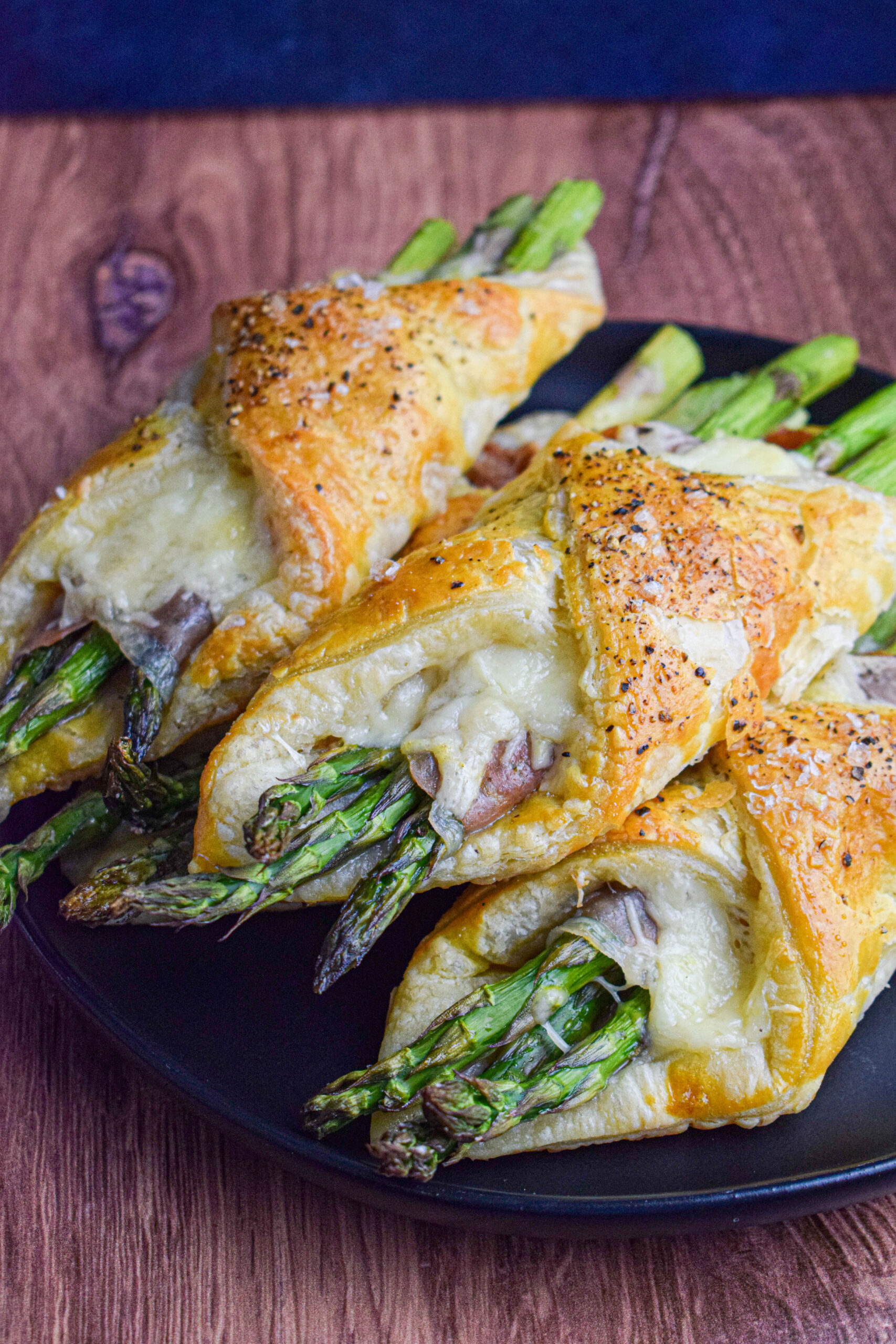 black plate with a stack of asparagus, prosciutto and cheese puff pastry tarts 