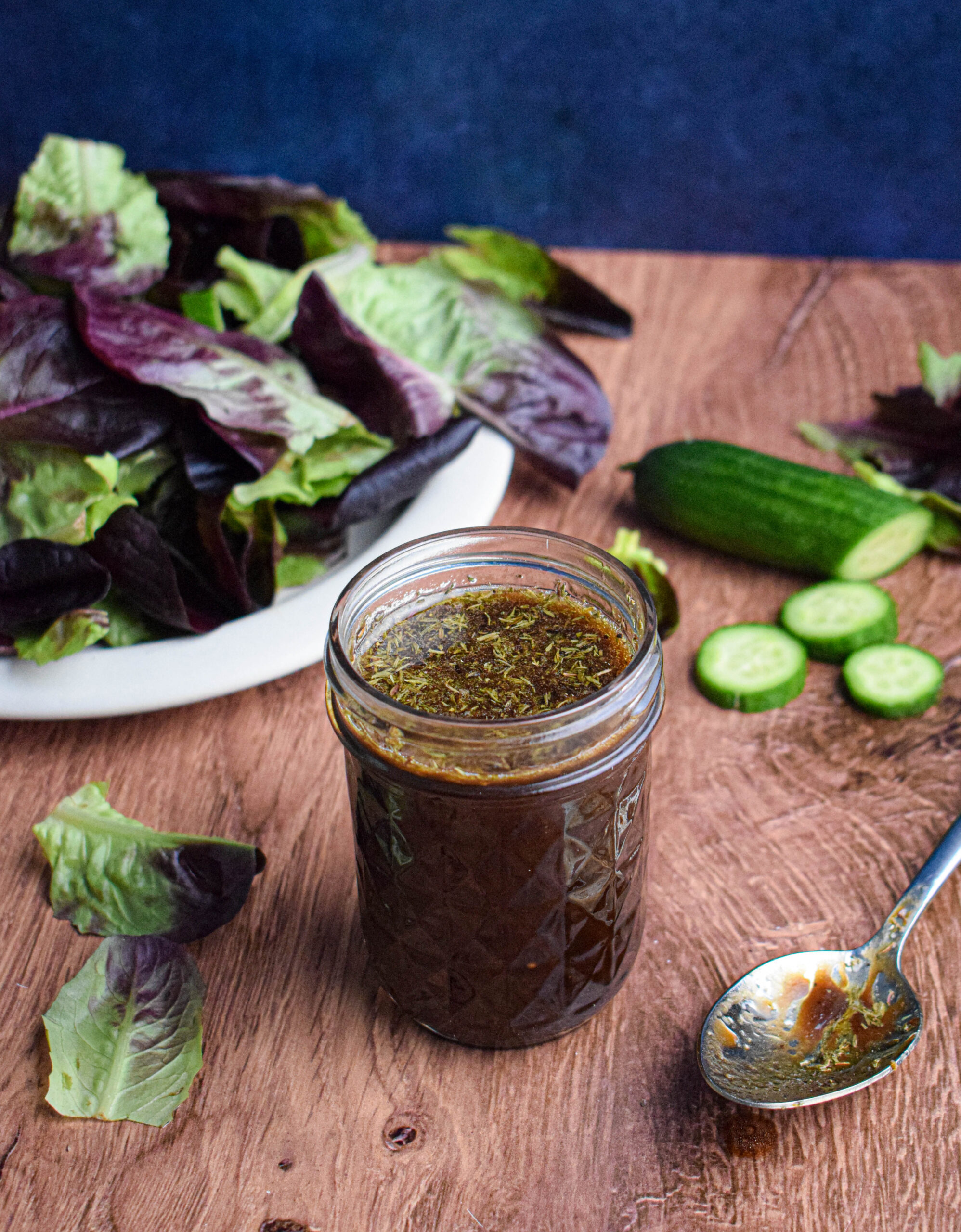 mason jar full of maple balsamic dressing surrounded by salad leaves and cucumber