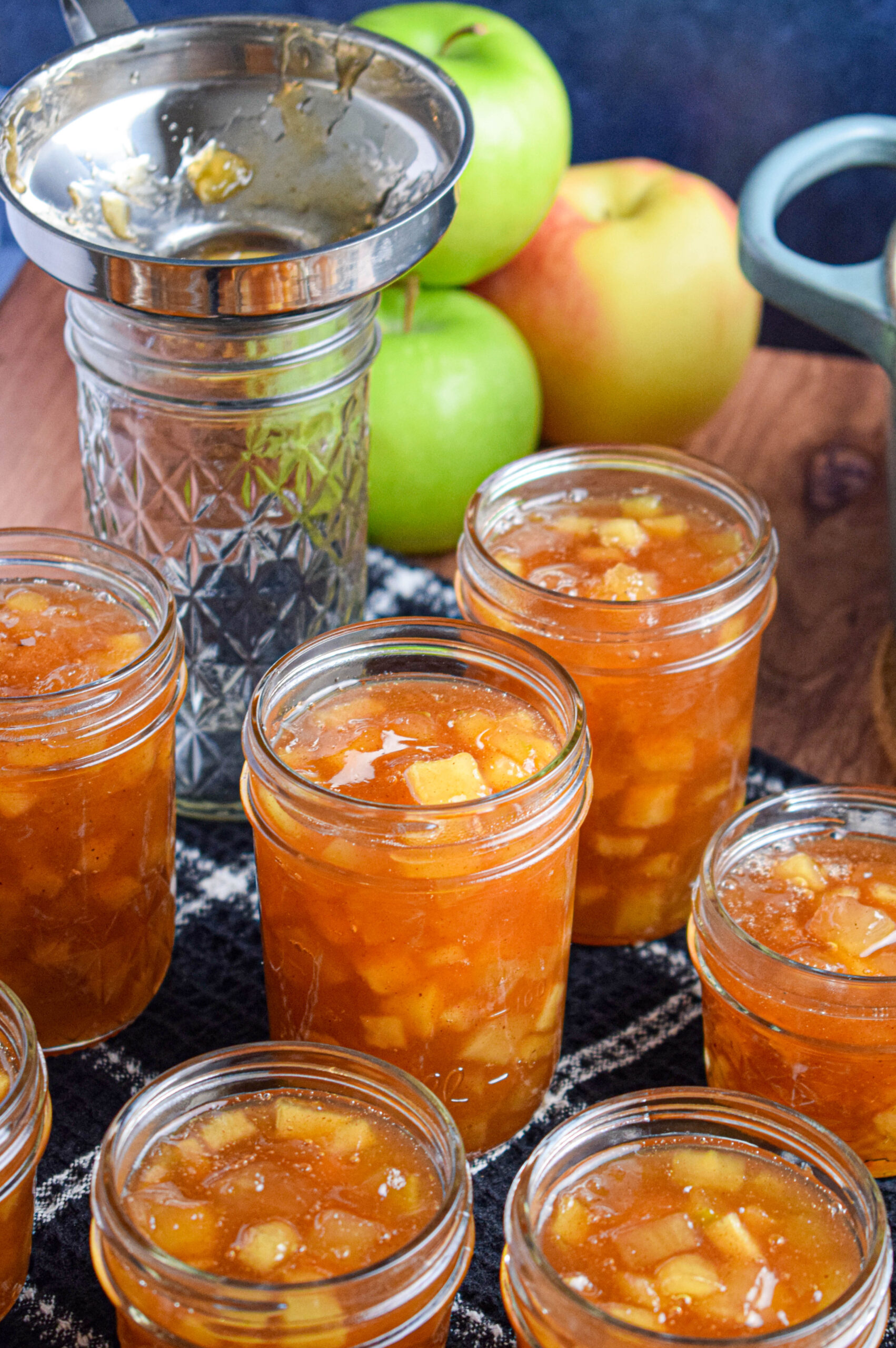 several jars full of apple pie jam in front of a pile of green apples 