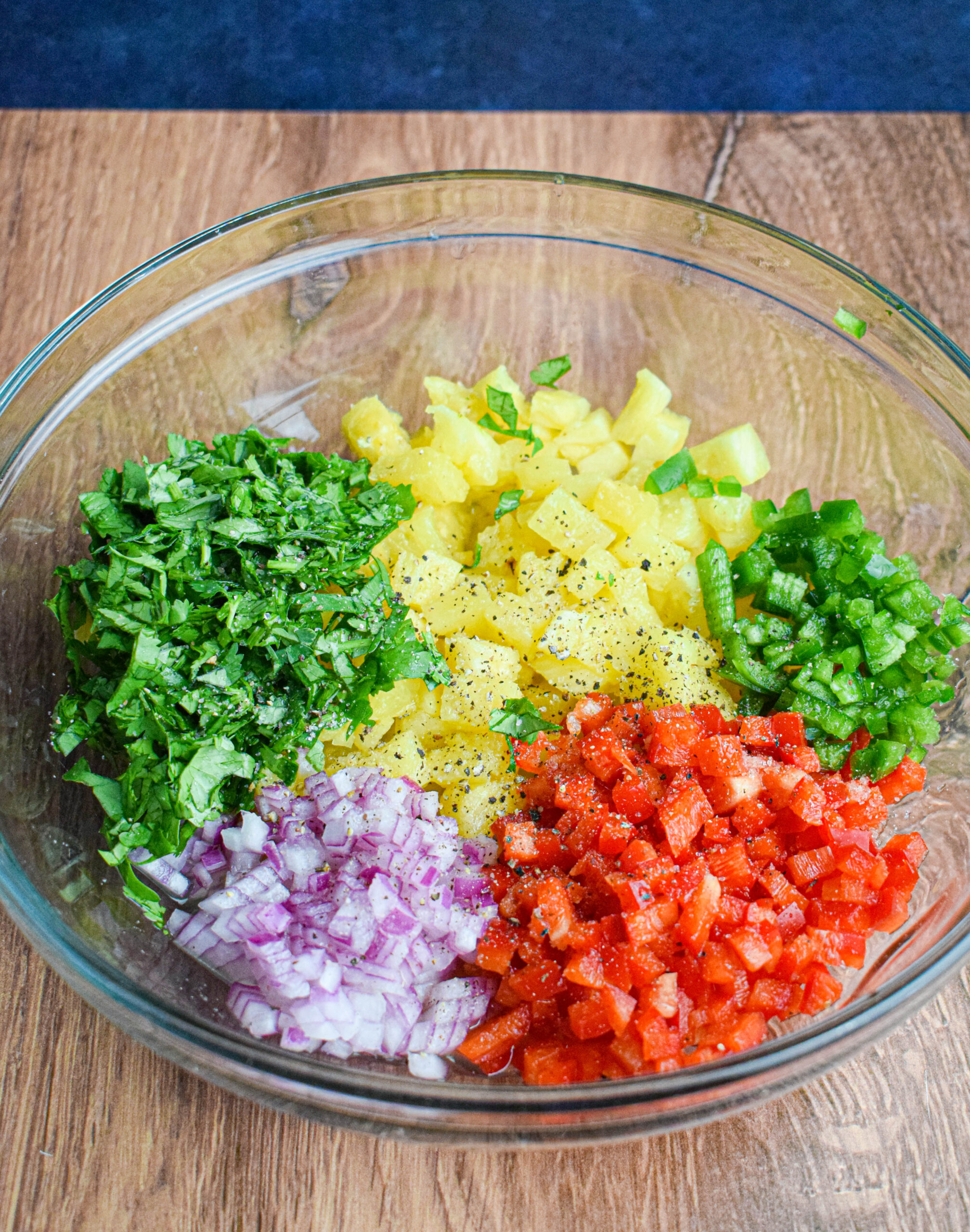 ingredients for pineapple pico de gallo chopped and arranged in a glass bowl. pineapple, red bell pepper, red onion, cilantro, lime. salt and pepper and jalapeno 