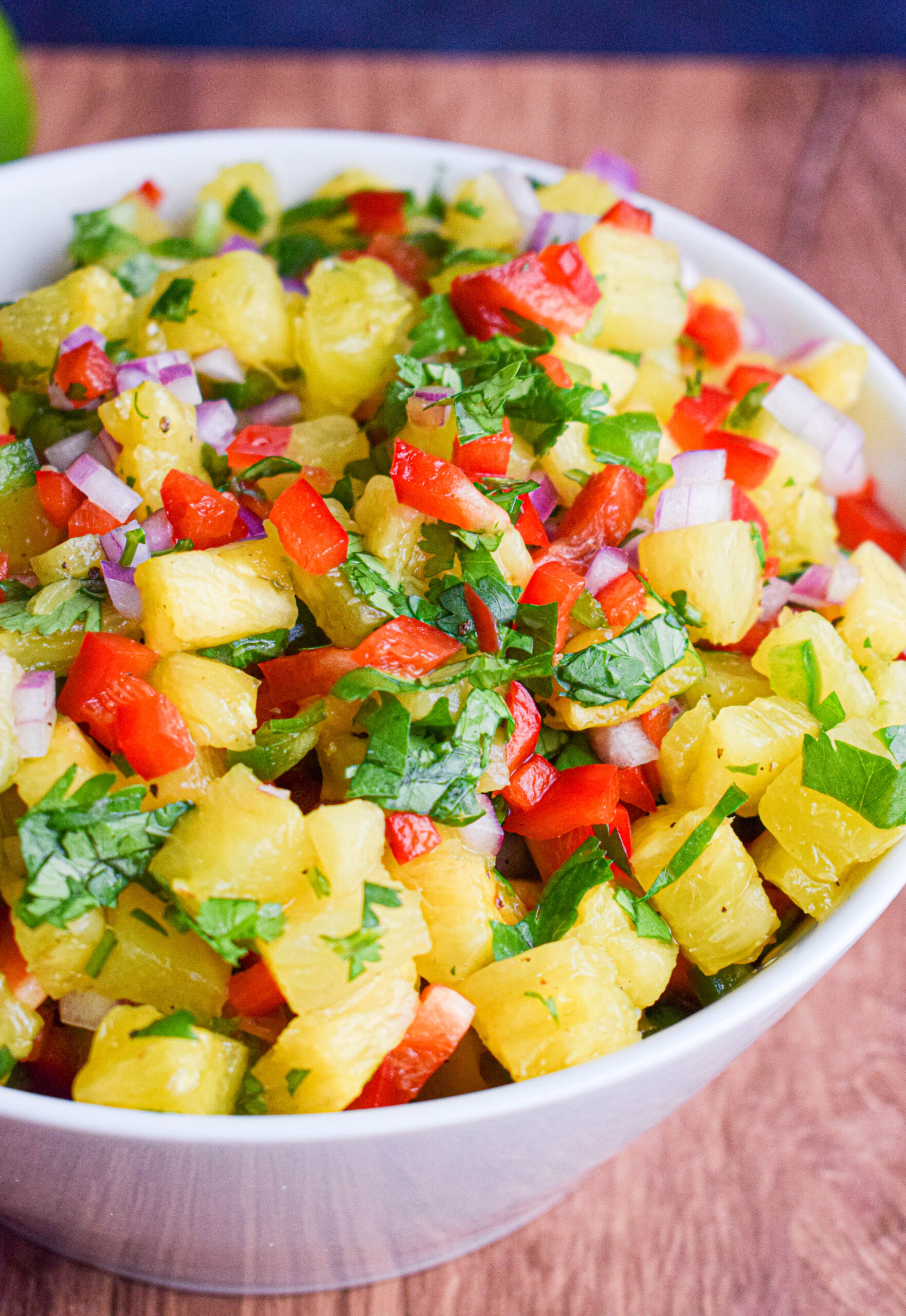 white bowl full of pineapple pico de gallo with red bell pepper, red onion, jalapeno and lime.