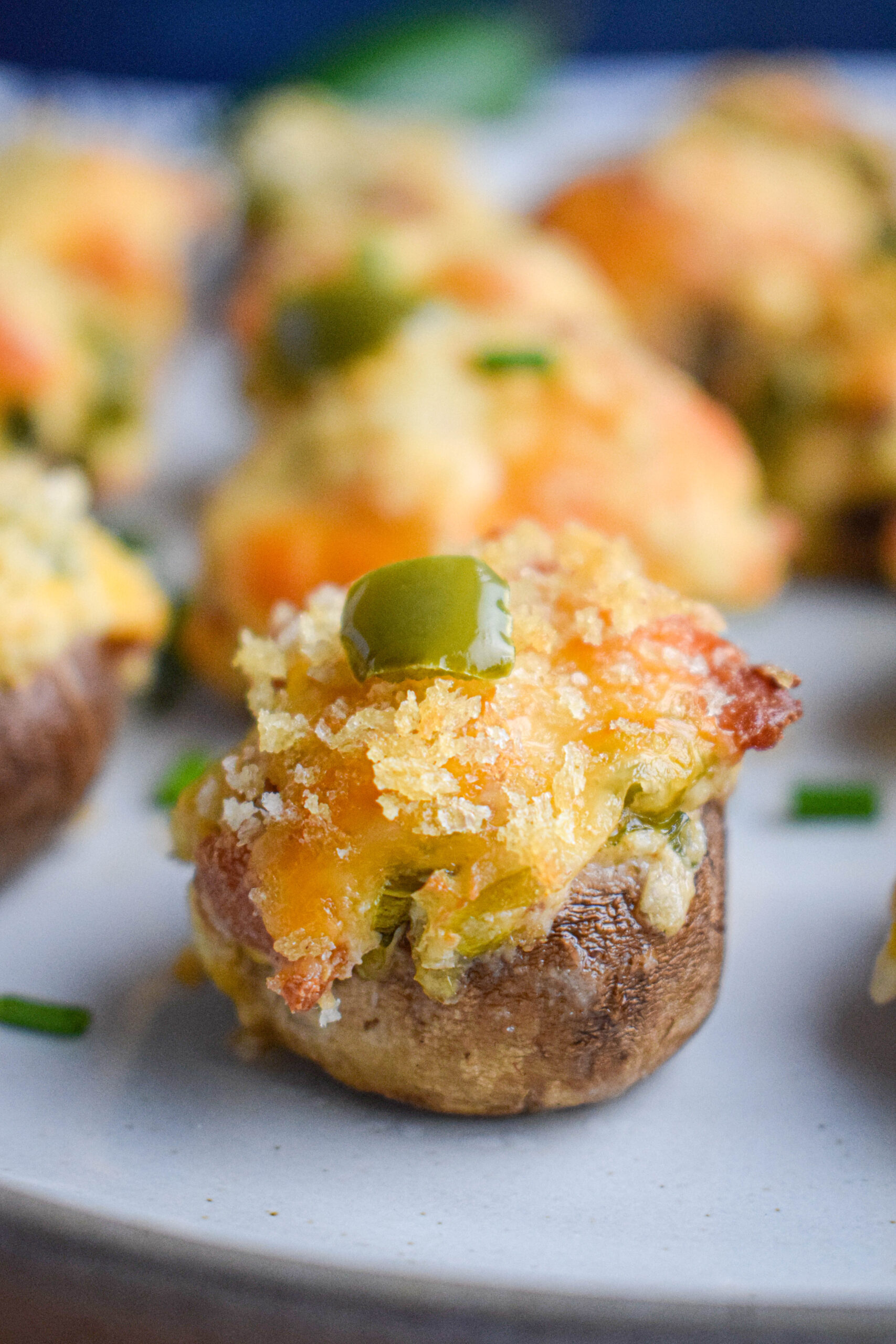 baked golden brown jalapeno bacon and cream cheese stuffed mushroom stopped with cheese, panko breadcrumbs and peppers