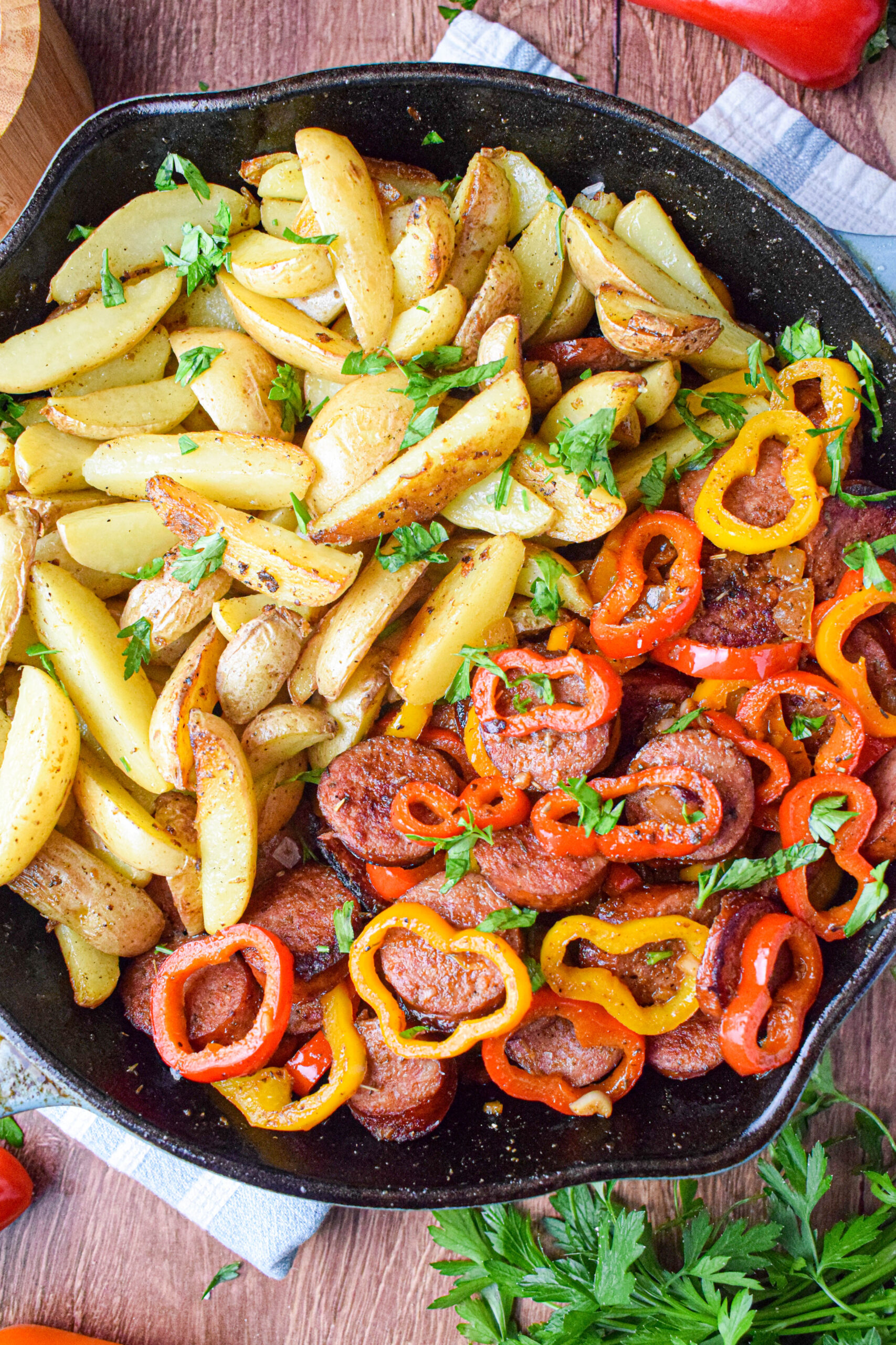cast iron skillet with potatoes, sausages and bell peppers topped with parsley
