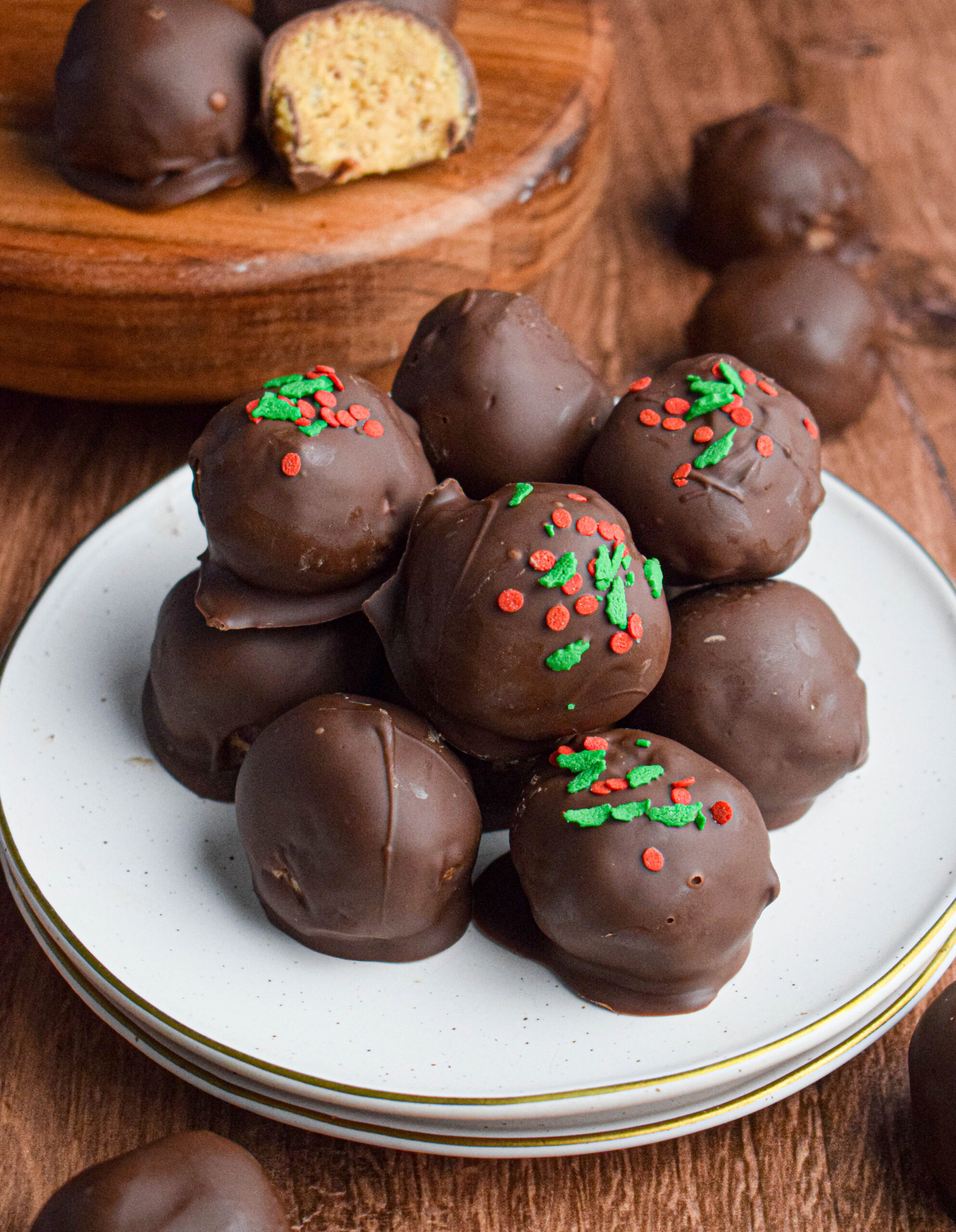 plate with a pile of chocolate covered peanut butter balls, some with holiday sprinkles, others plain