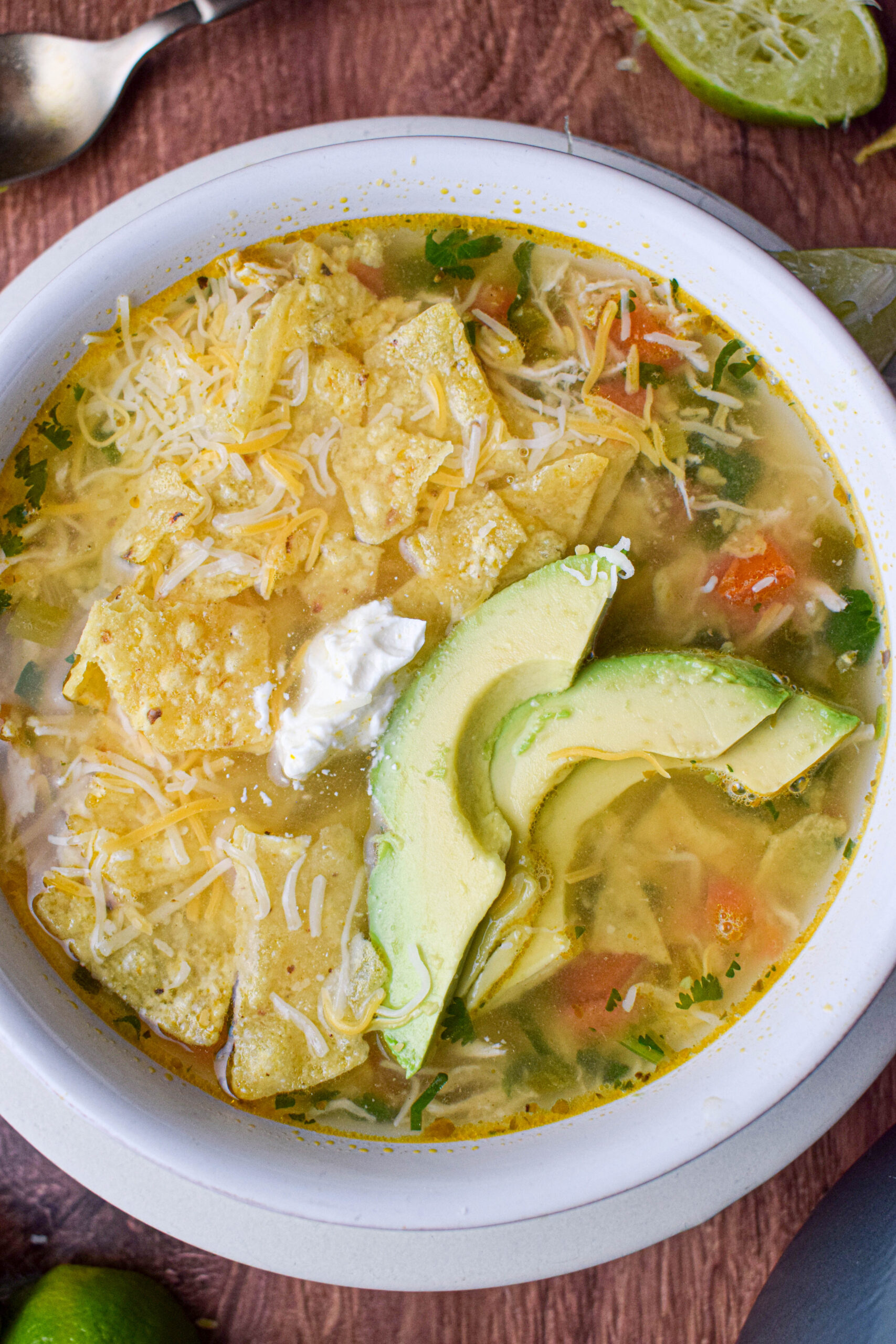 close up shot of chicken and lime soup with toppings avocado, sour cream and tortilla 