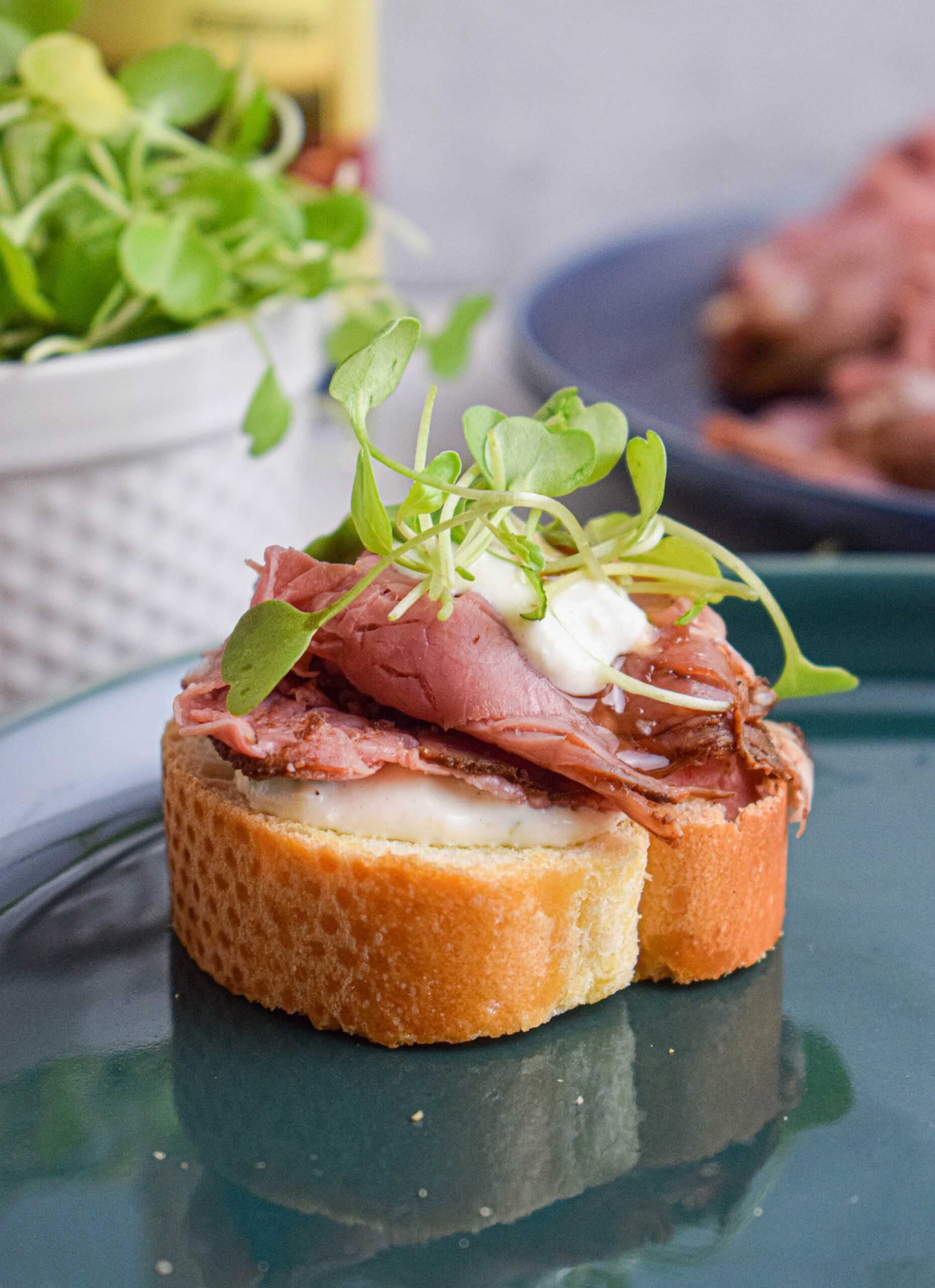 green plate with a single holiday crostini with roast beef, horseradish sauce and arugula