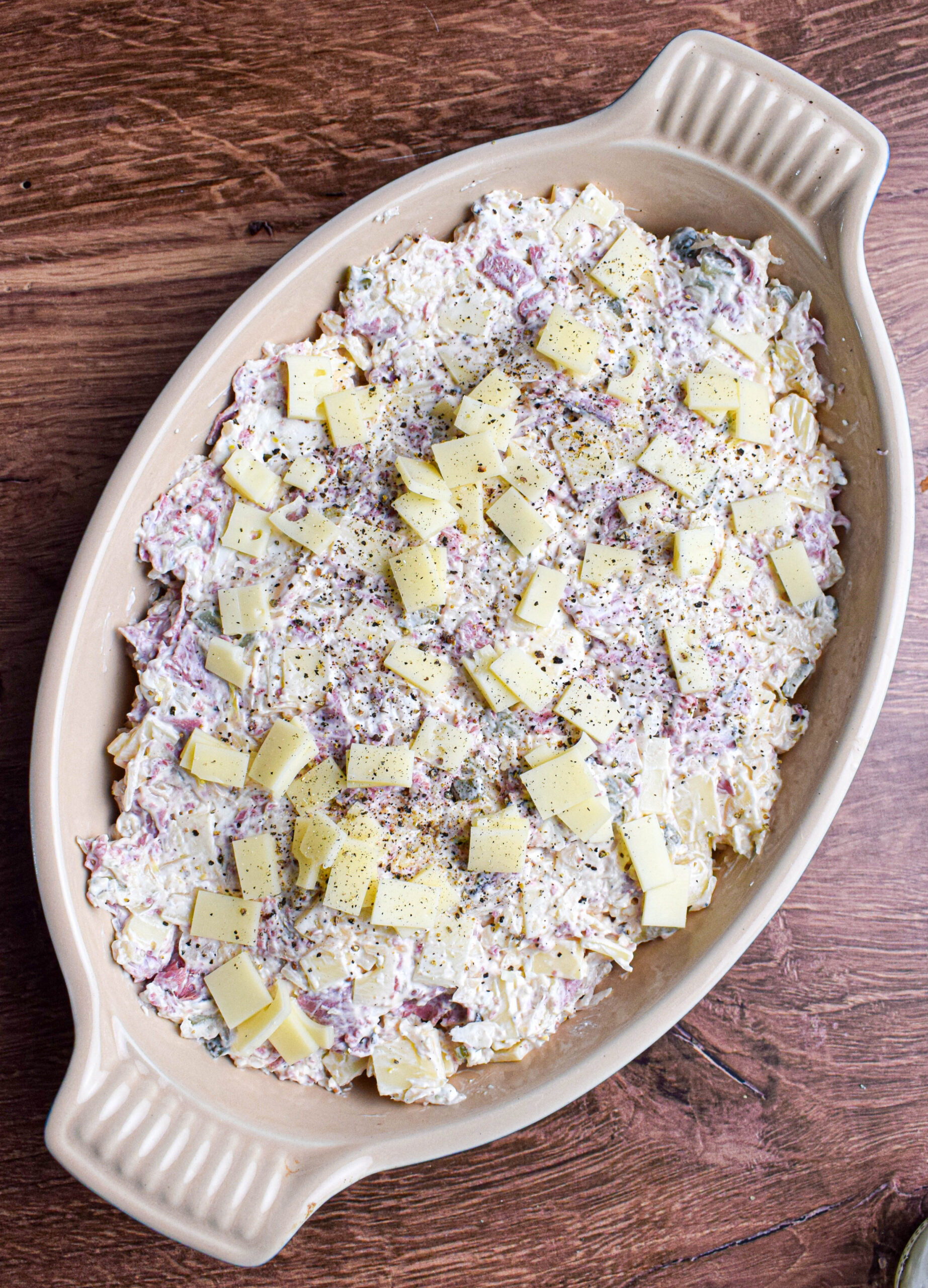 An overhead shot of unbaked dip with pastrami and cubed Swiss cheese on top.