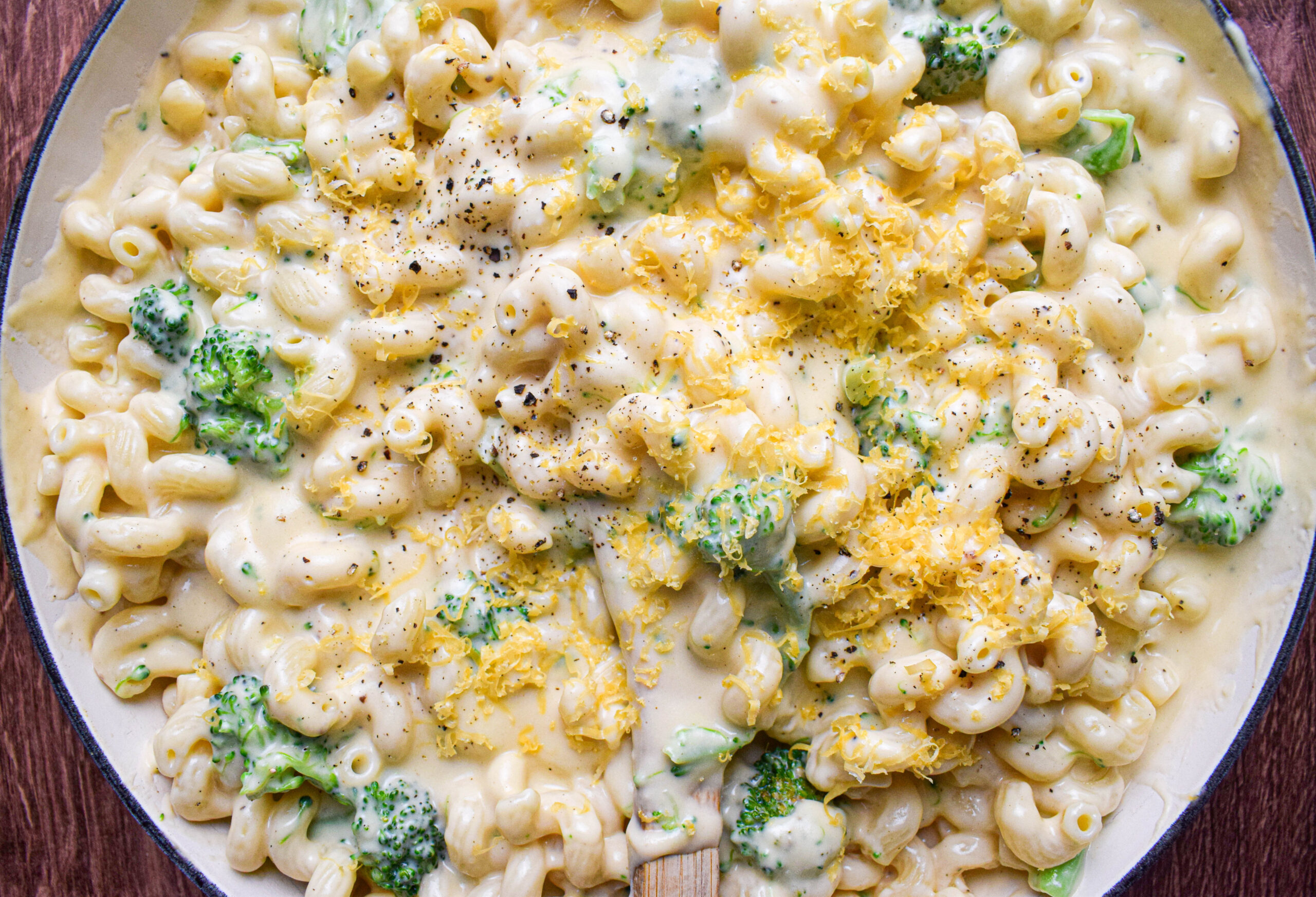 Overhead shot of a pan full of creamy stovetop macaroni and cheese with broccoli topped with shredded cheddar cheese and freshly cracked black pepper.