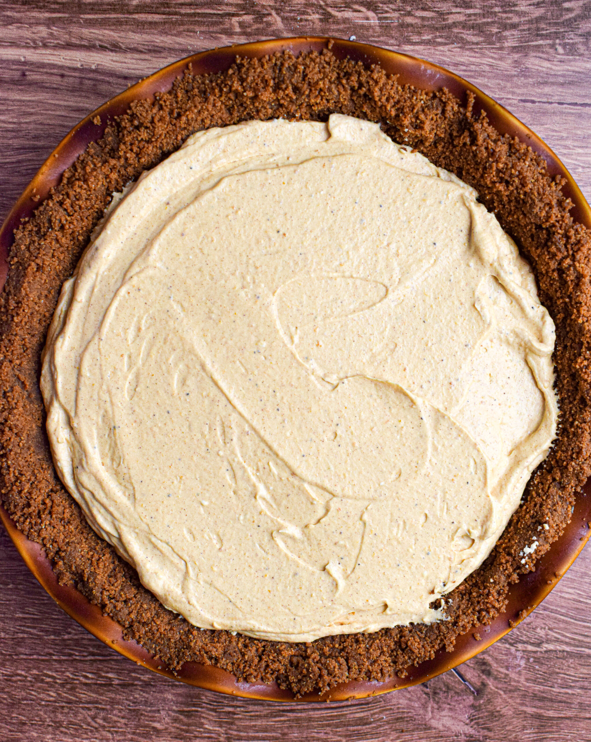 Overhead shot of a brown pie dish filled with no bake pumpkin cheesecake mousse in a ginger snap crust.