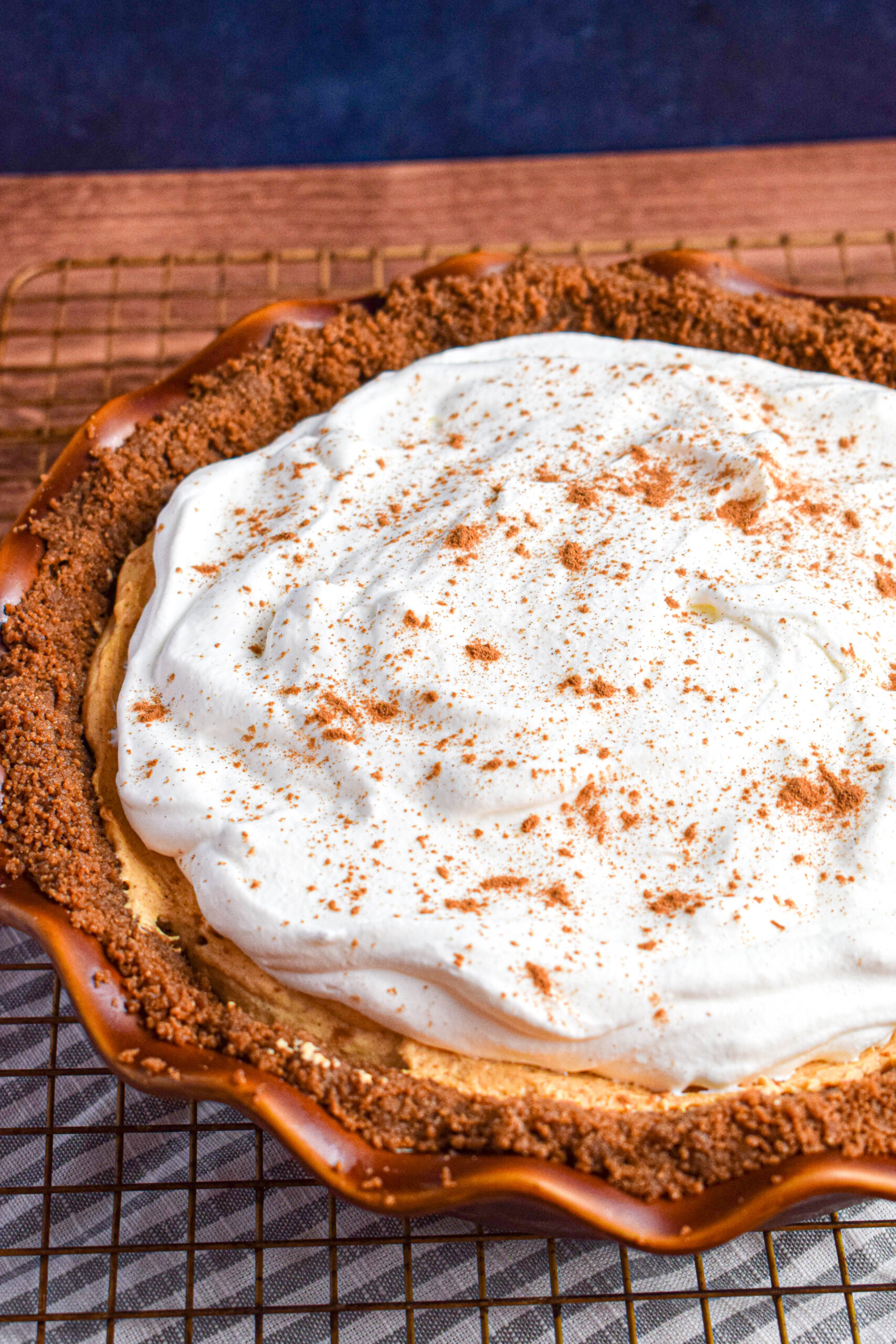 Tilted angle shot of a finished pumpkin mousse pie in a brown pie pan topped with whipped cream and cinnamon. 