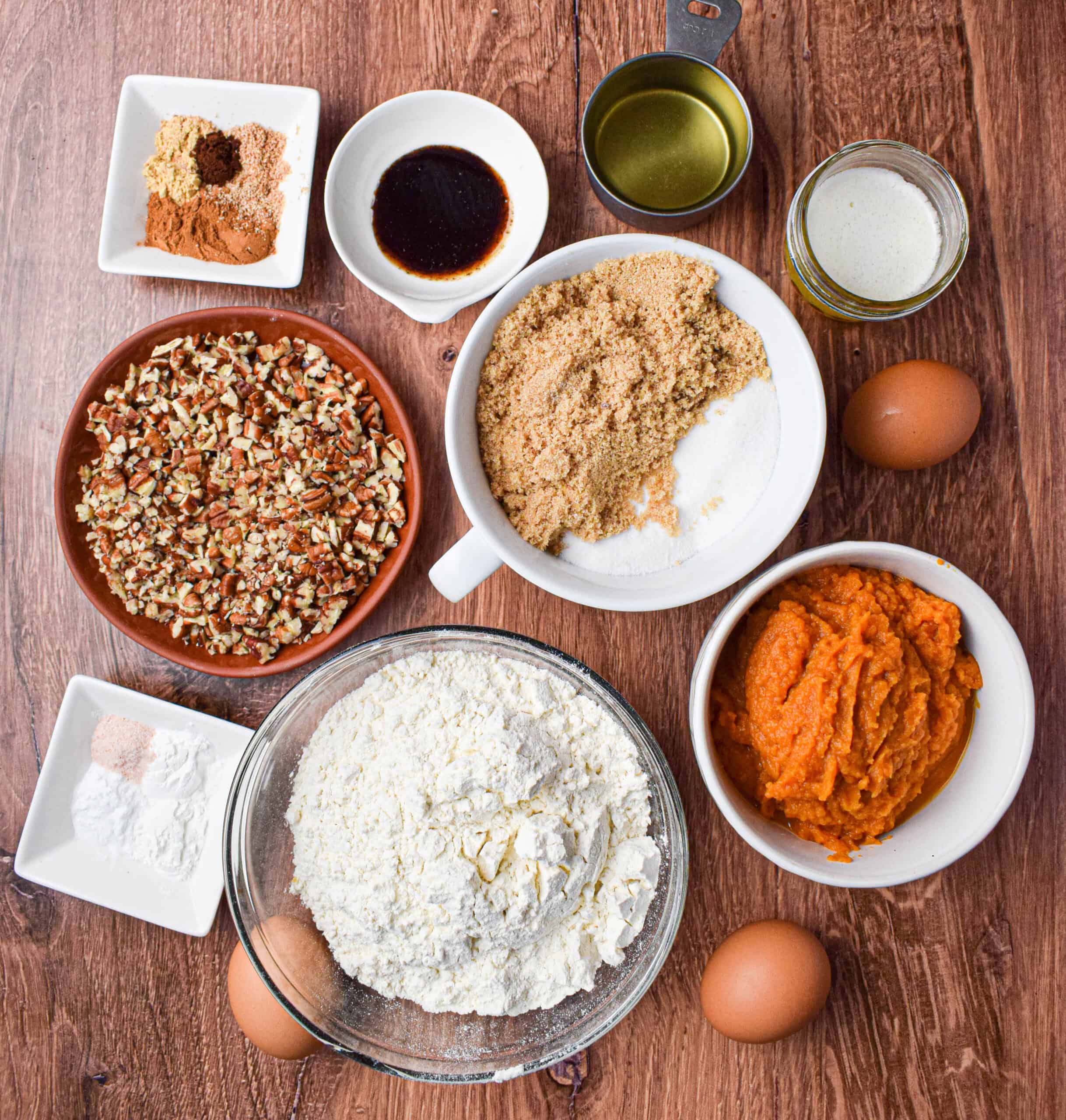 Overhead shots showing the ingredients for pumpkin pecan bread including: chopped pecans, brown and white sugar, spices, vanilla extract, oil, melted butter, baking soda and powder, pumpkin puree, flour and eggs. 