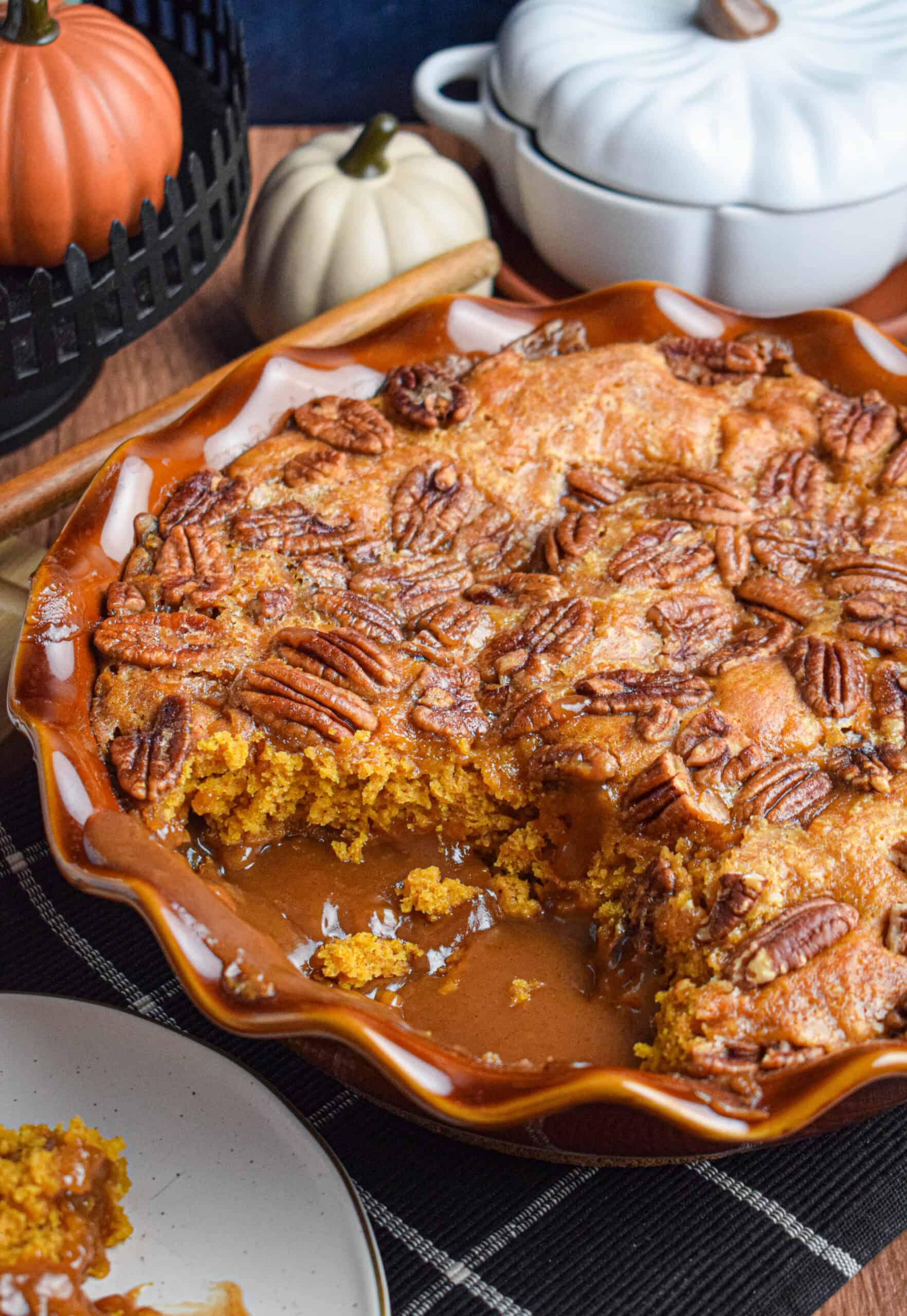 A brown pie dish is full or pumpkin cobbler with pecans and an ooey gooey brown sugar sauce. 