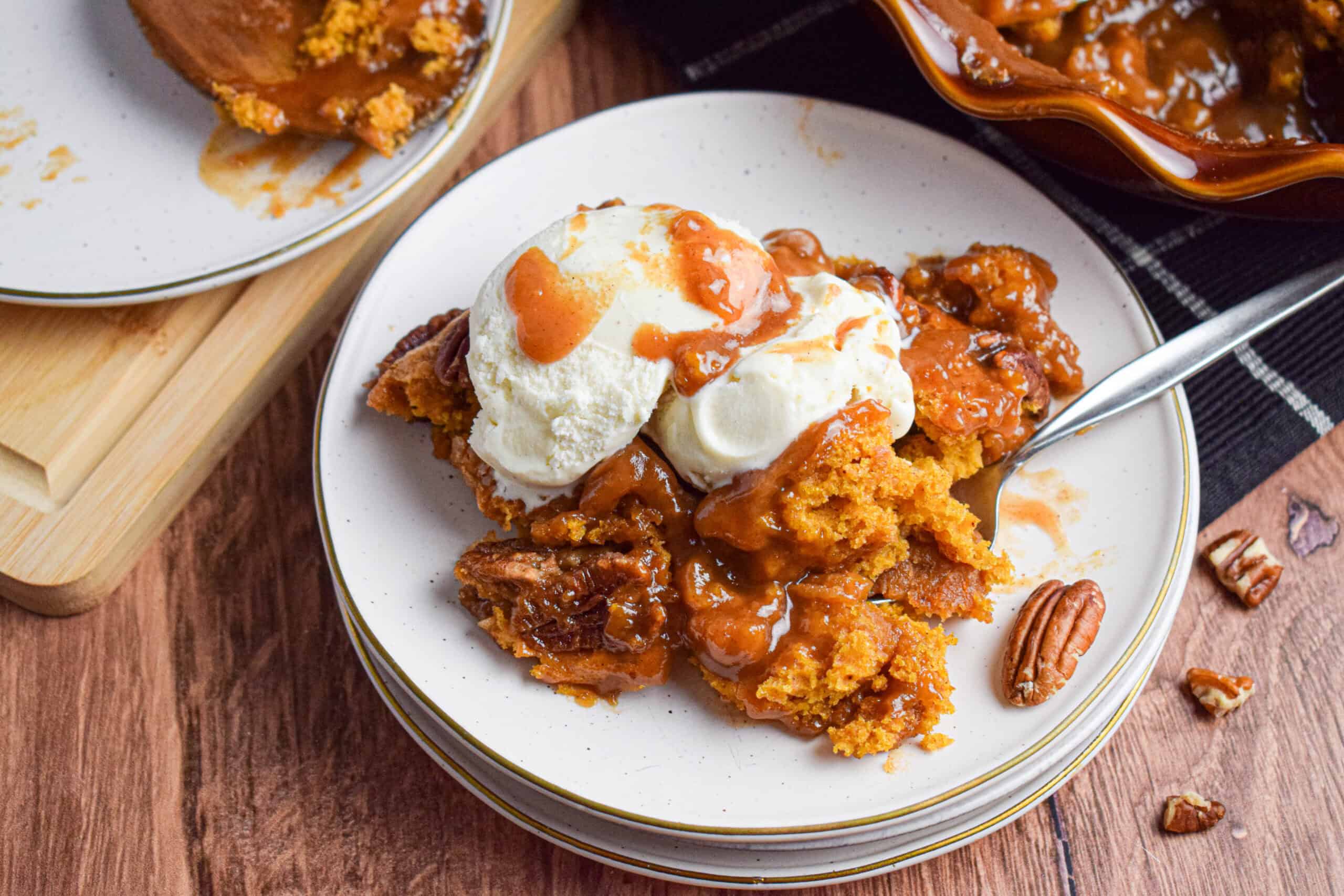 A serving of pumpkin cobbler is on a stack of white plates topped with ice cream and a brown sugar sauce. 