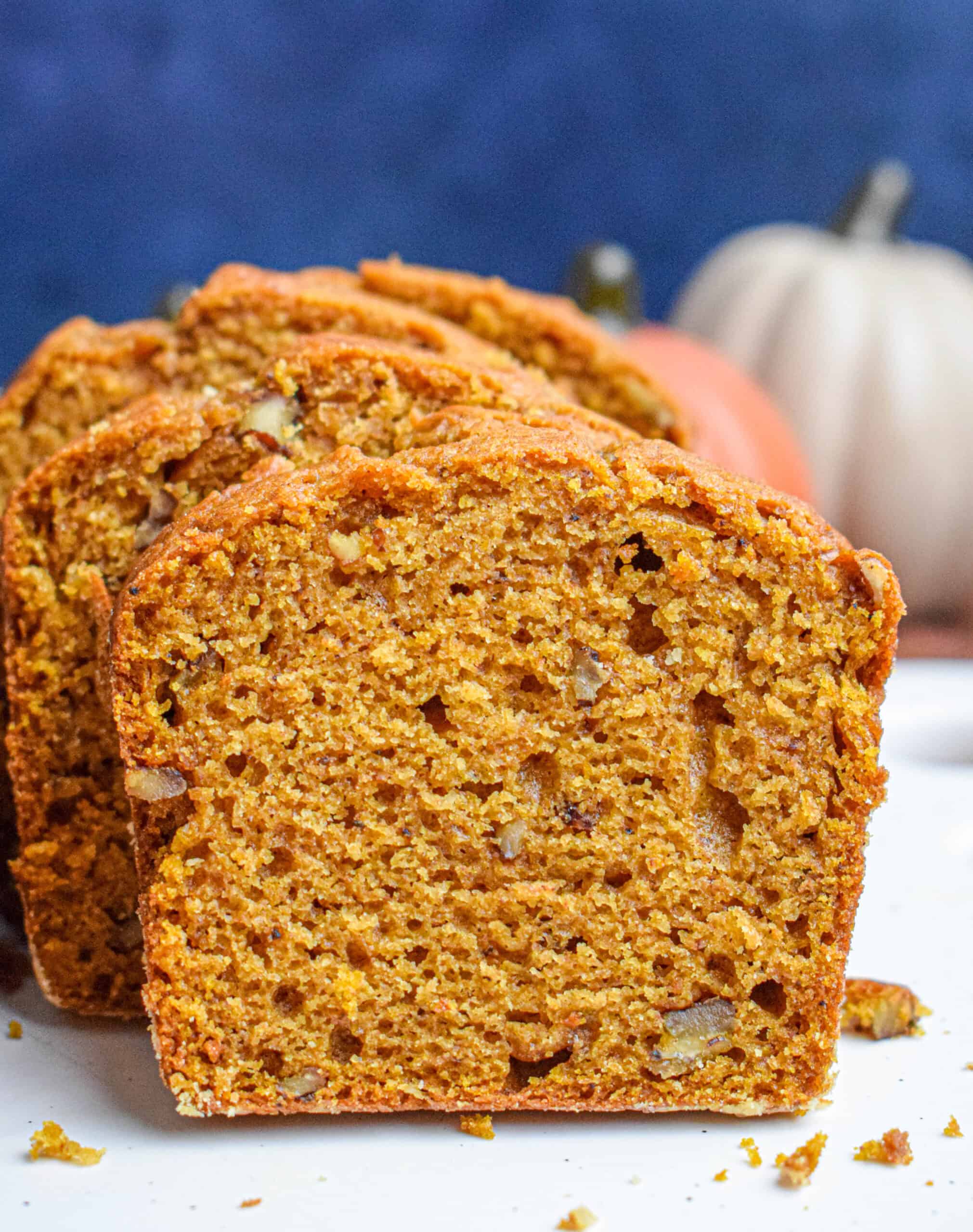 Close up of a slice of pumpkin bread showing a moist but light orang-ish crumb studded with pecans. 