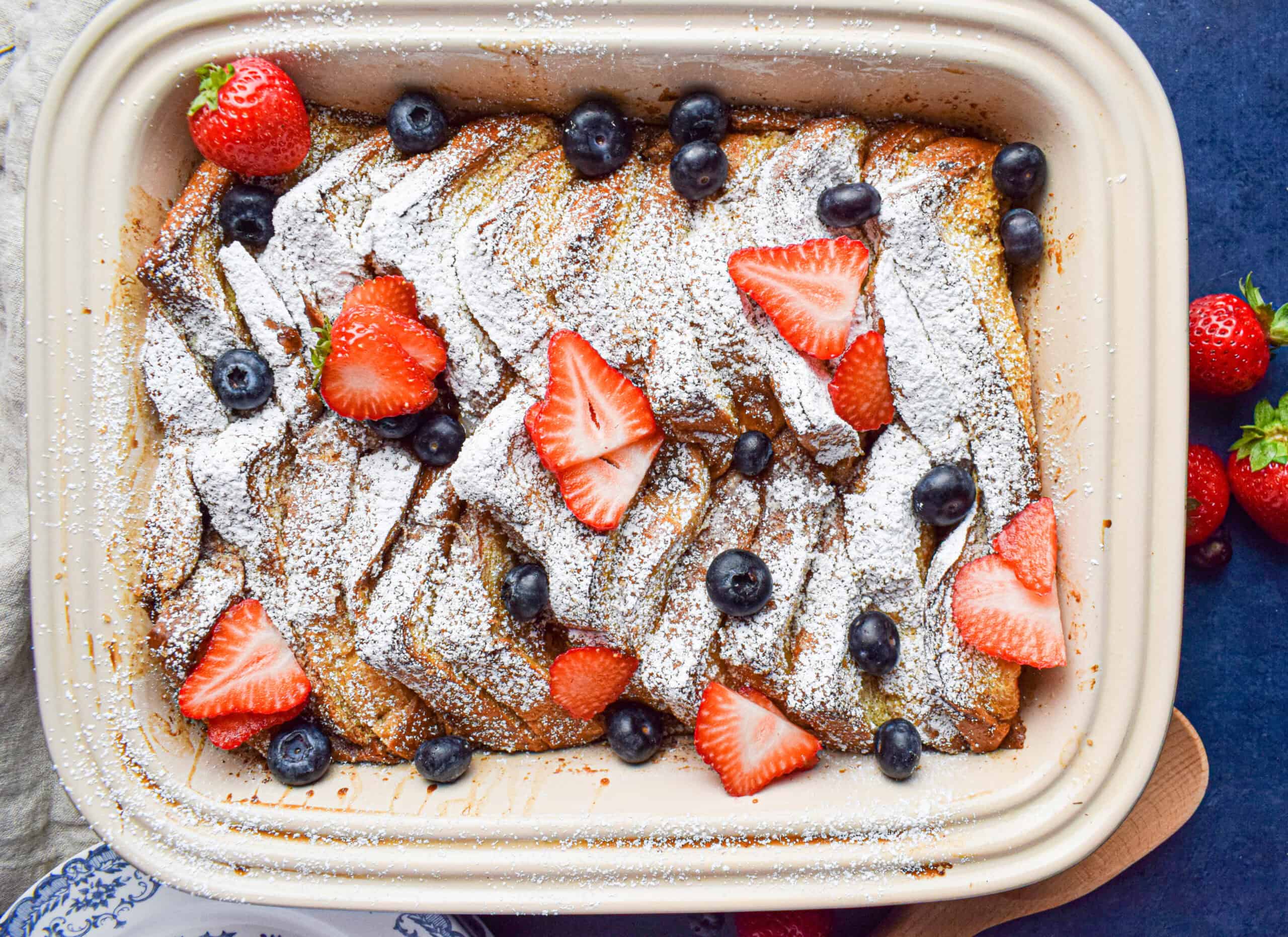A large baking dish filled with the best brioche french toast casserole topped with powdered sugar and berries. 