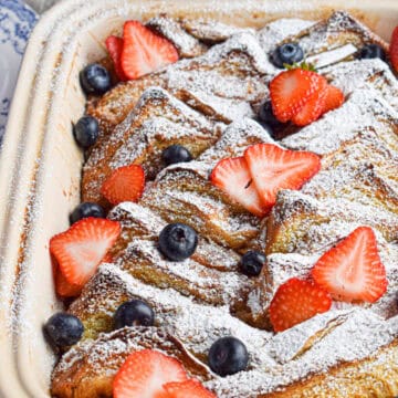 Brioche french toast casserole topped with sugar and berries in a large casserole dish.