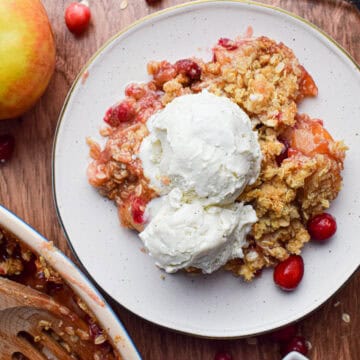 apple and cranberry crumble on a white plate surround by ingredients.