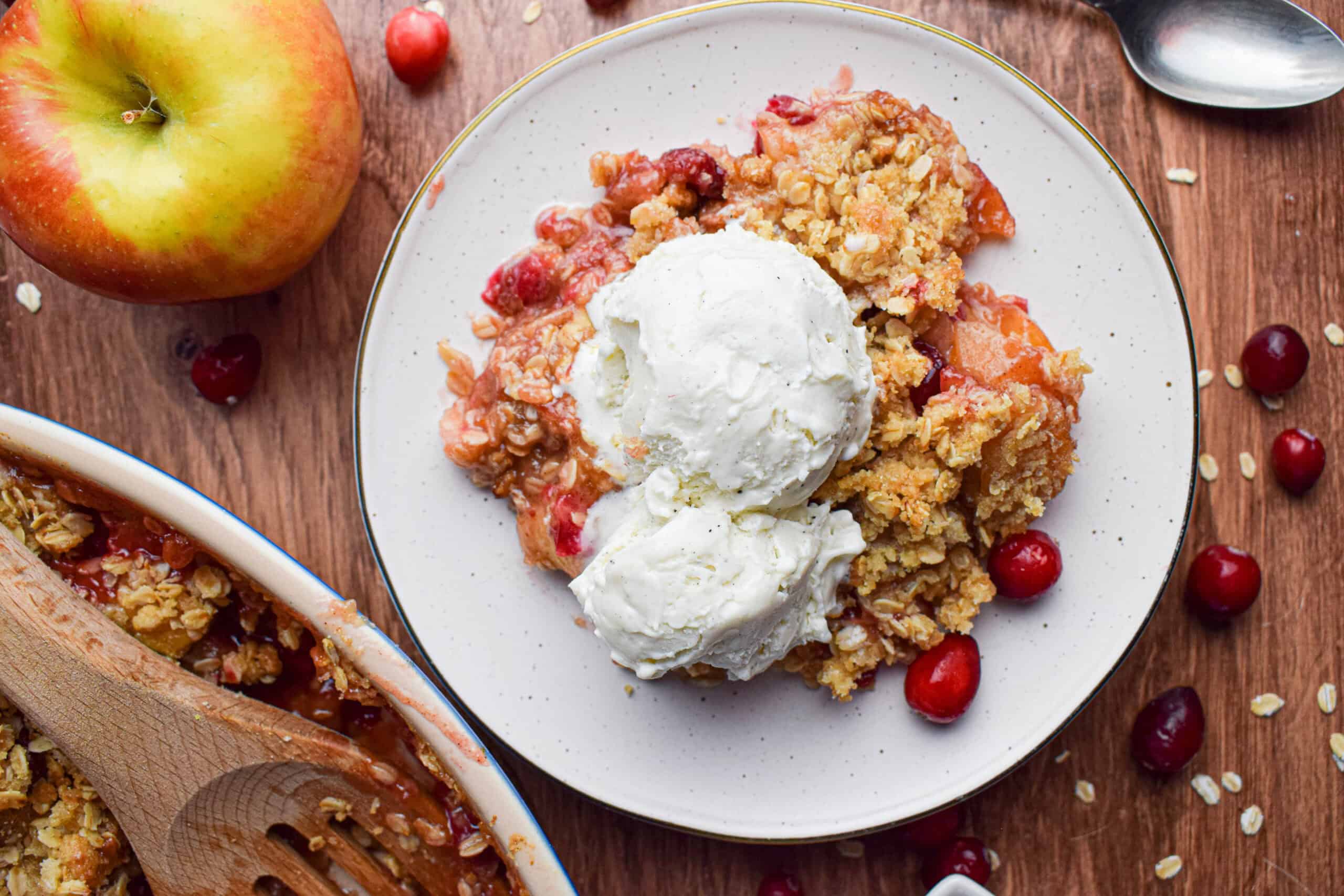 Overhead shot showing a serving of apple and cranberry crumble crisp on a white plate topped with vanilla ice cream.