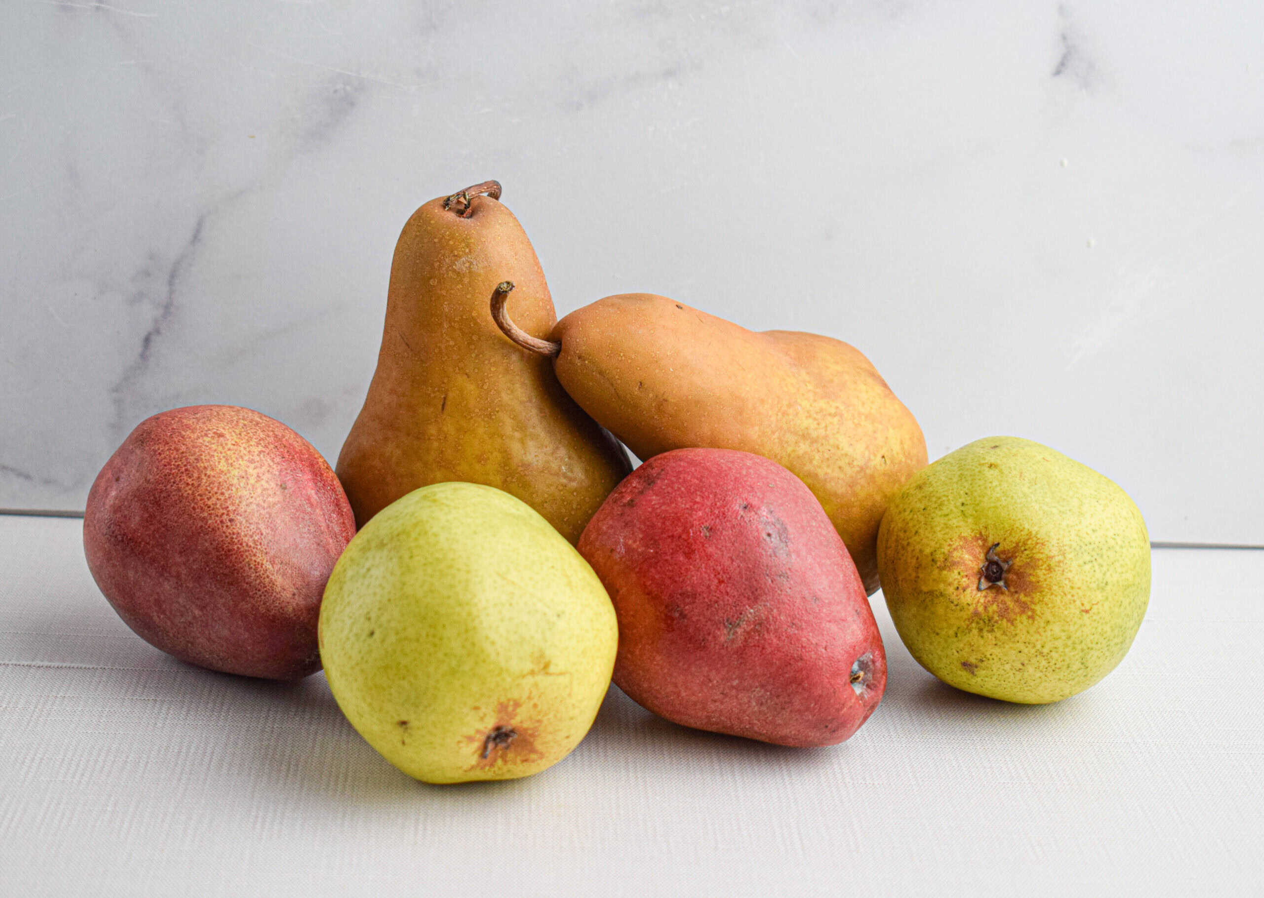 Pears of varying shapes and colors are sitting in front of a white backdrop. 