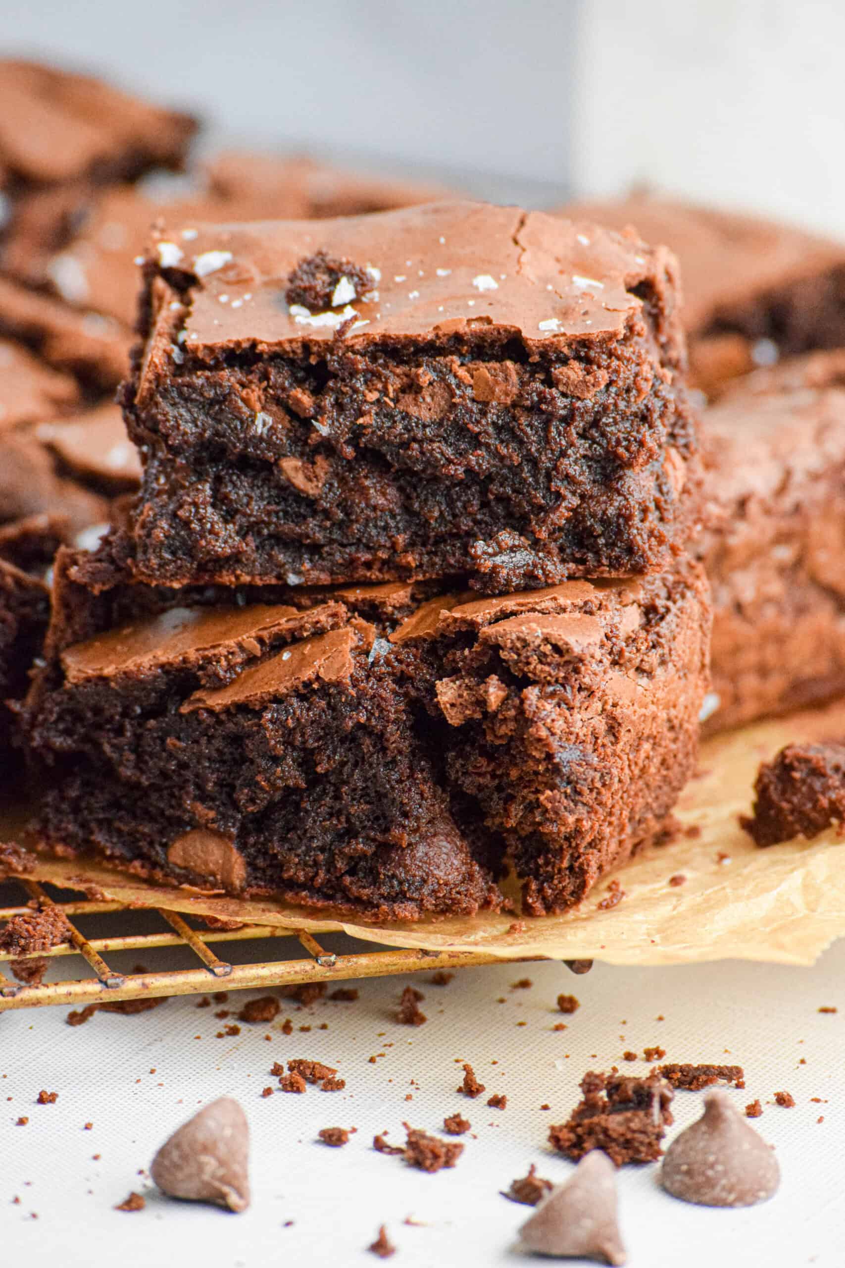 Two chocolate brownies made with sourdough starter are stacked on top of each other on a cooling rack, showing a gooey, fudge chocolatey center and a crackly top. 