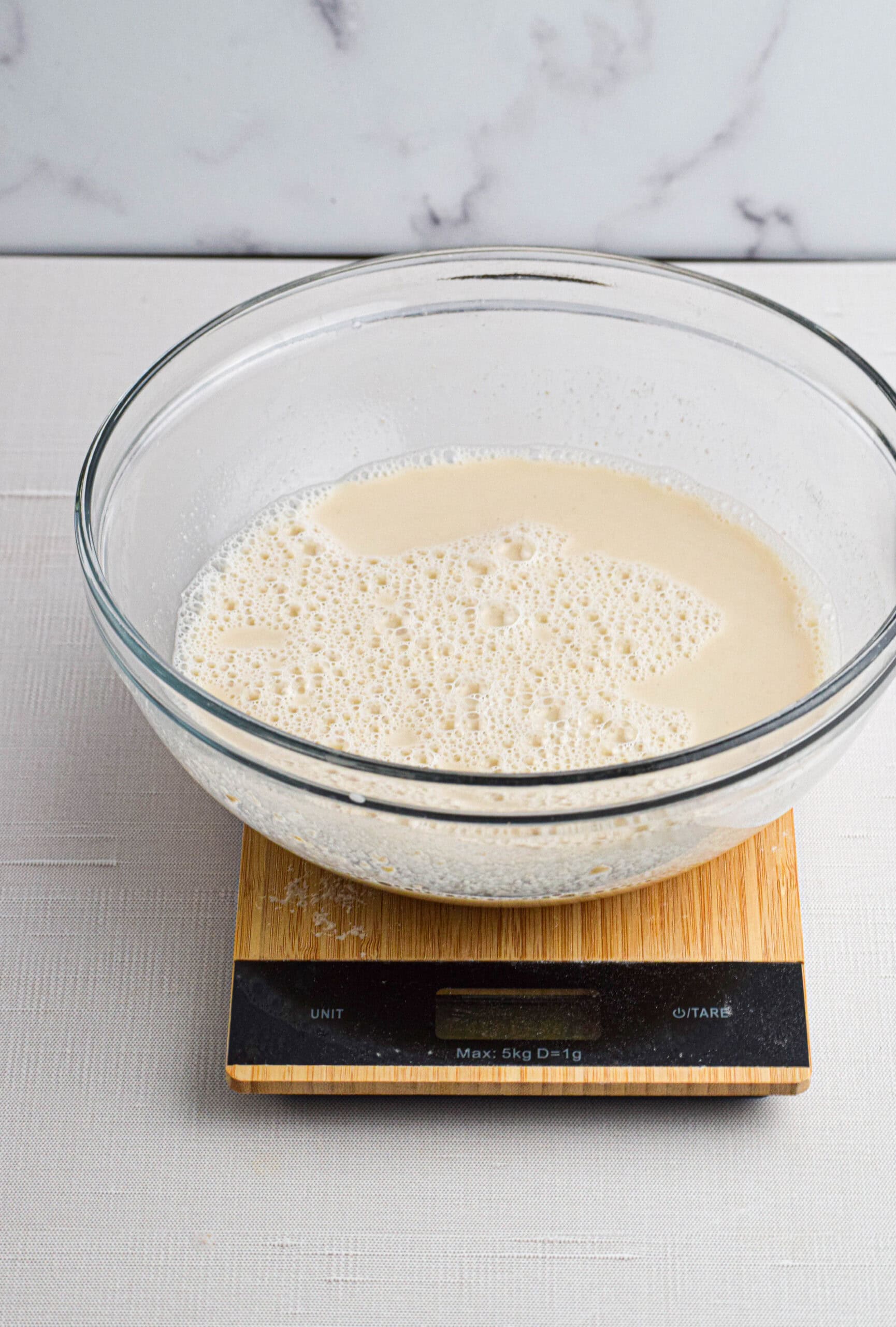 A glass bowl on a kitchen scale full of sourdough starter mixed with water. 