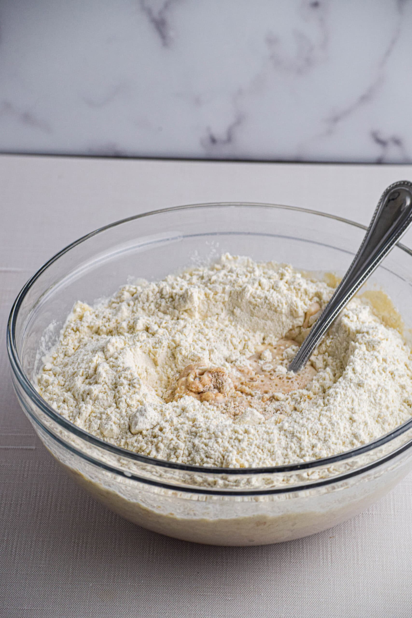 A glass bowl with unmixed starter, water, flour and salt. 