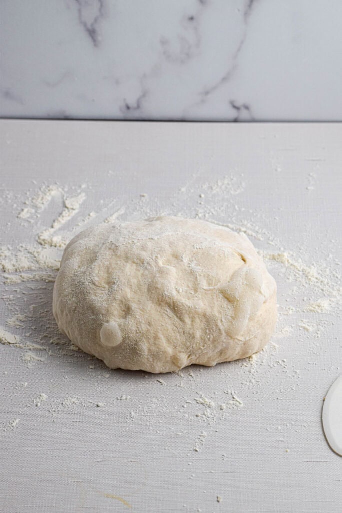 The bread dough has been shaped and sits on a floured surface. 