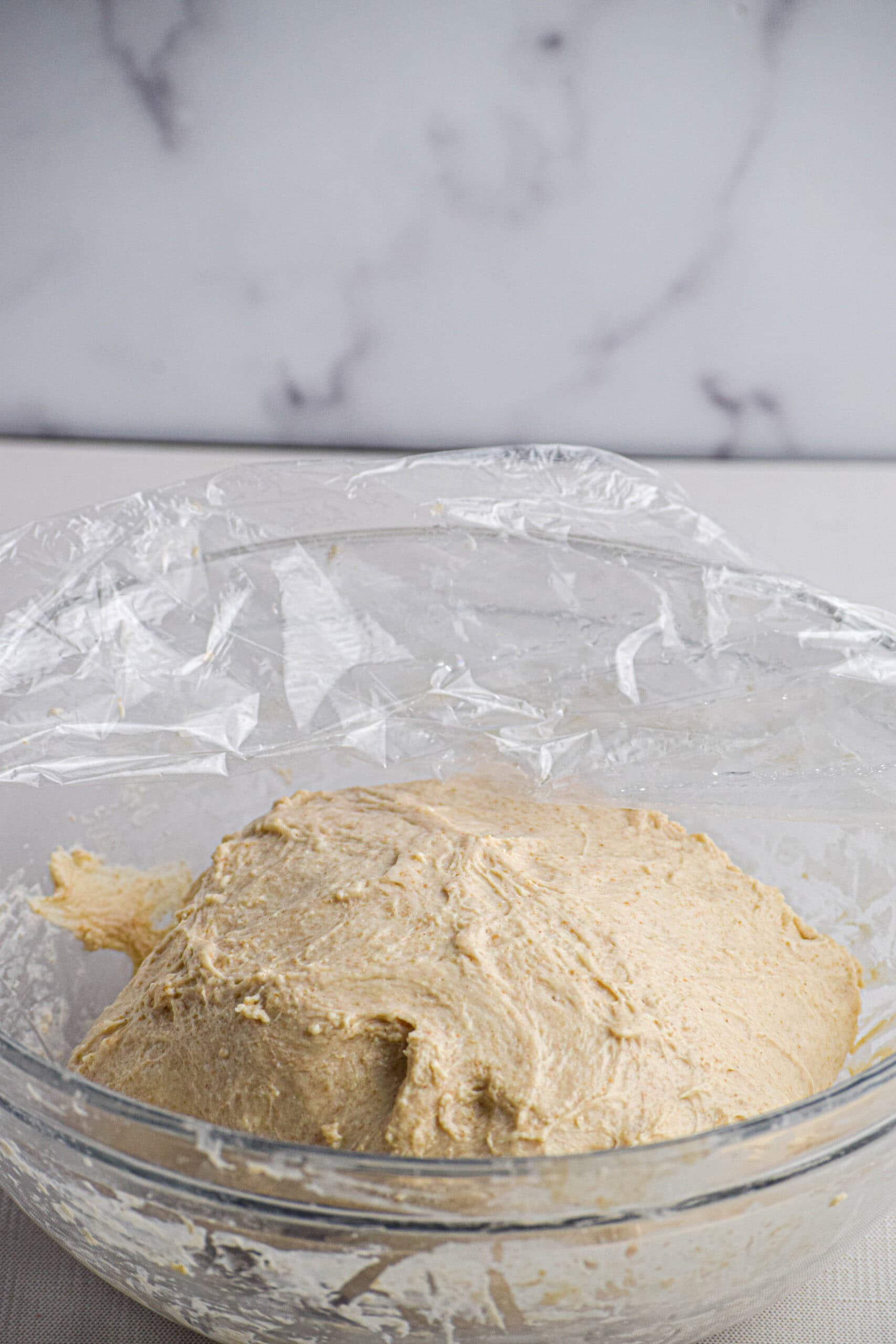 a glass bowl soughdough dough that has gone through several series of stretches and fold with a piece of plastic wrap over it. 