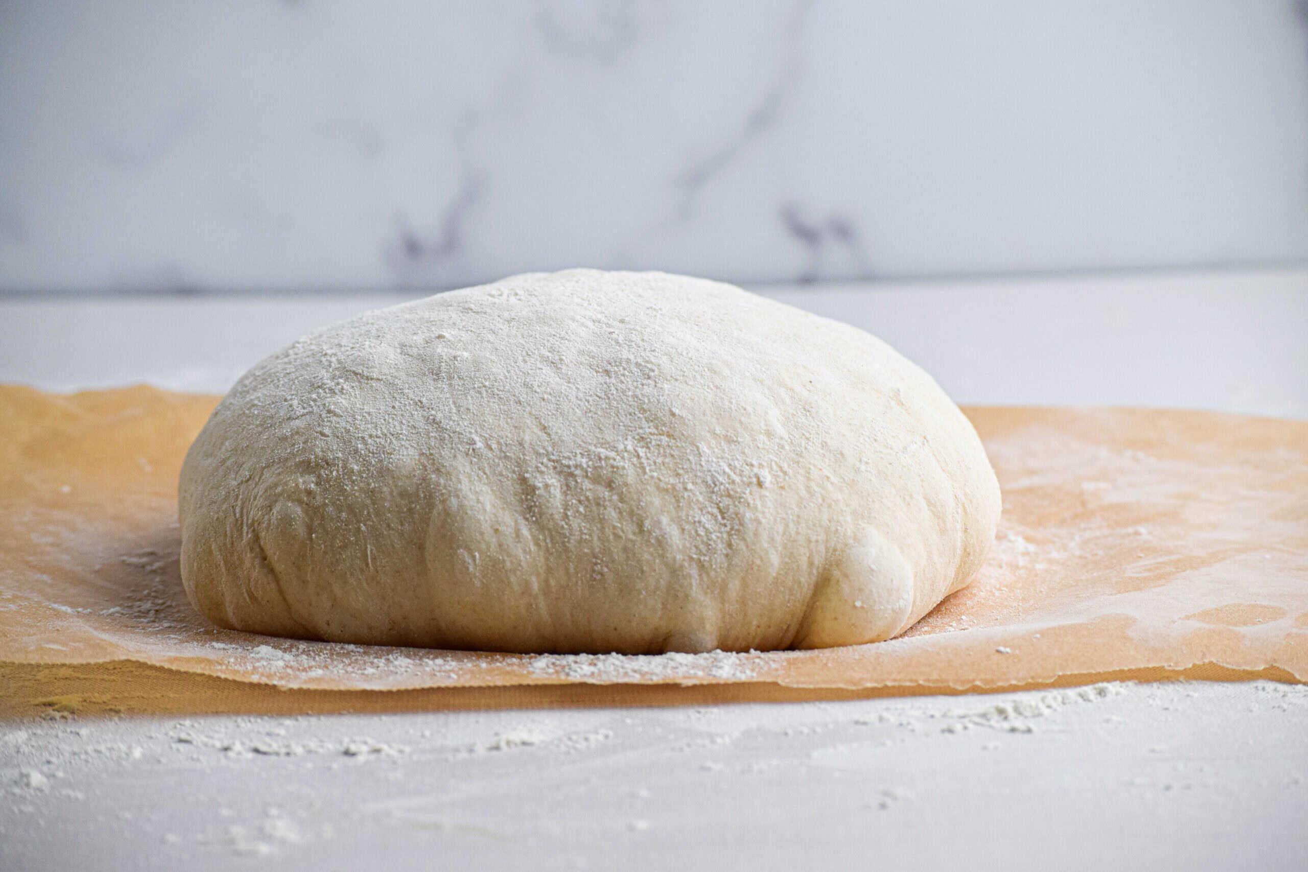 An unbaked but shaped sourdough loaf on a piece of floured parchment paper. 