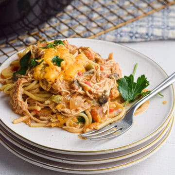 stacked plates with a serving of slow cooker chicken spaghetti topped with melted cheddar cheese
