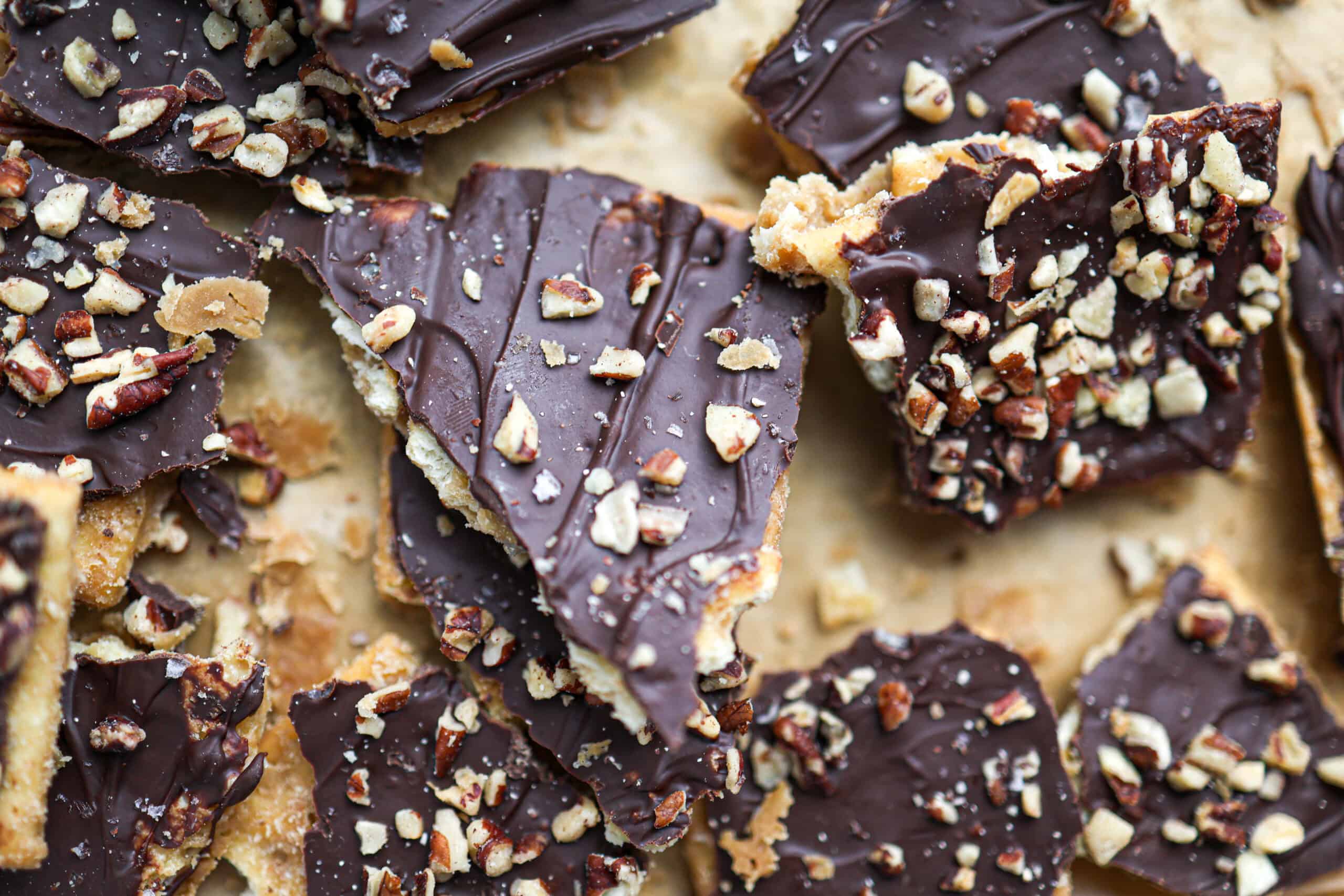 Close-up of chocolate toffee bark, also known as christmas crack, topped with chopped nuts and broken into irregular pieces on a light surface.