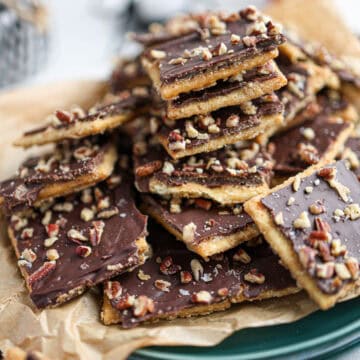 A plate of chocolate-covered toffee bark pieces, often called Christmas crack, topped with chopped nuts and arranged on parchment paper.