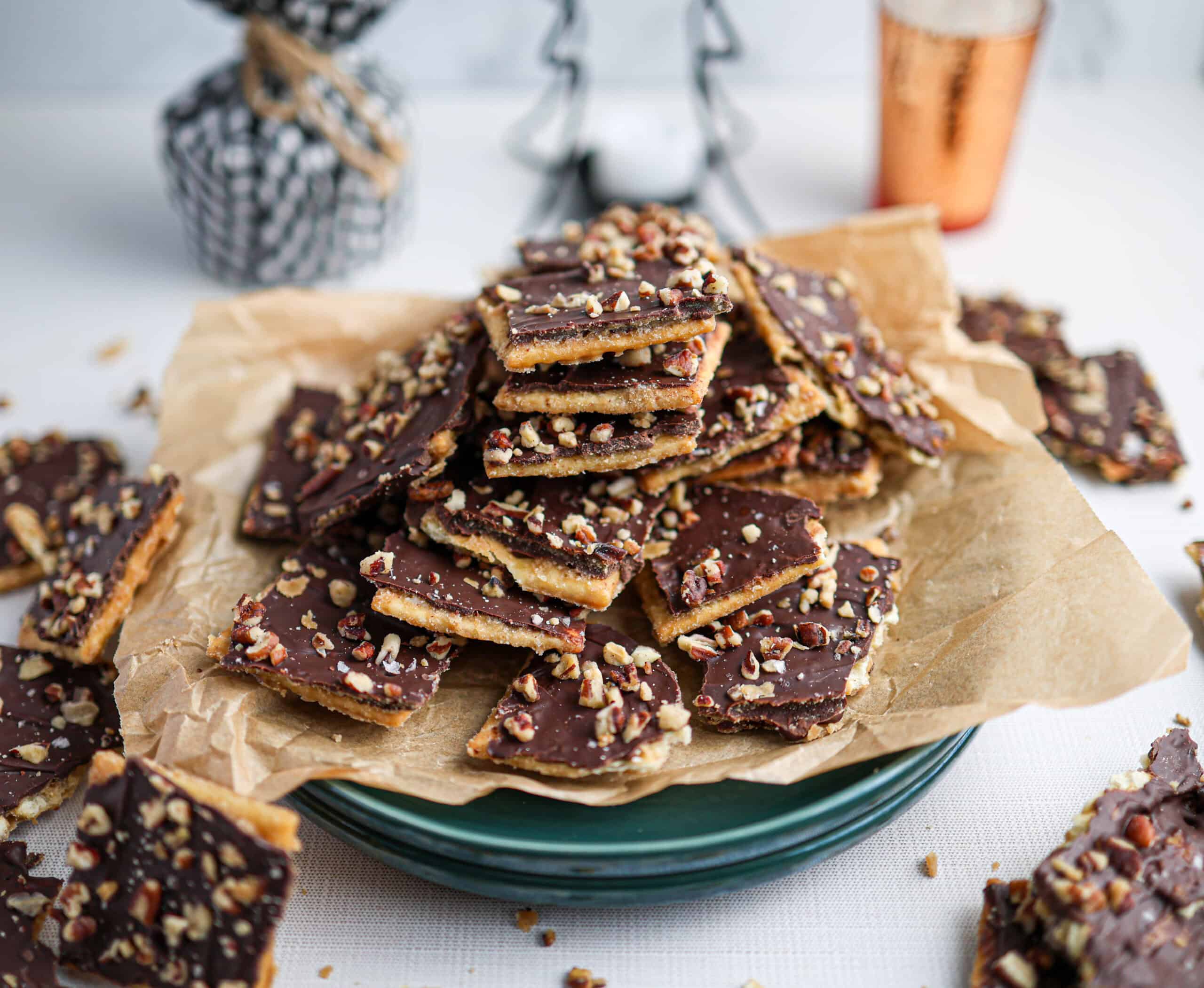 A plate stacked with homemade chocolate toffee bark, also known as Christmas crack, topped with chopped nuts and displayed on parchment paper.
