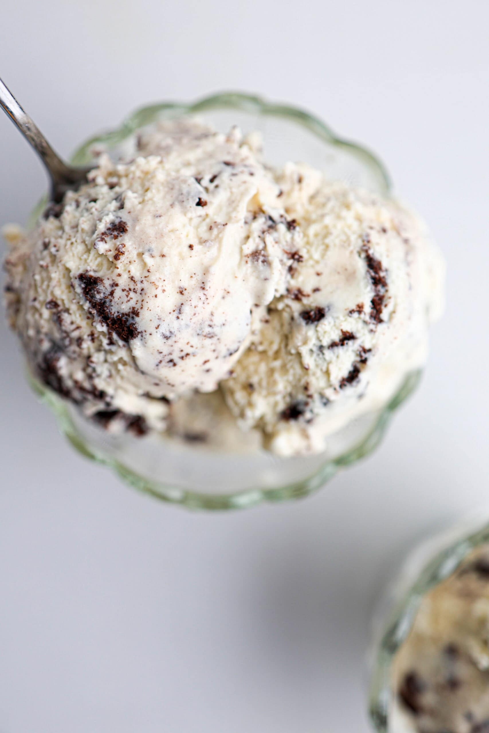 A close-up of a glass bowl filled with creamy cookies and cream ice cream, with a spoon scooping a generous portion.