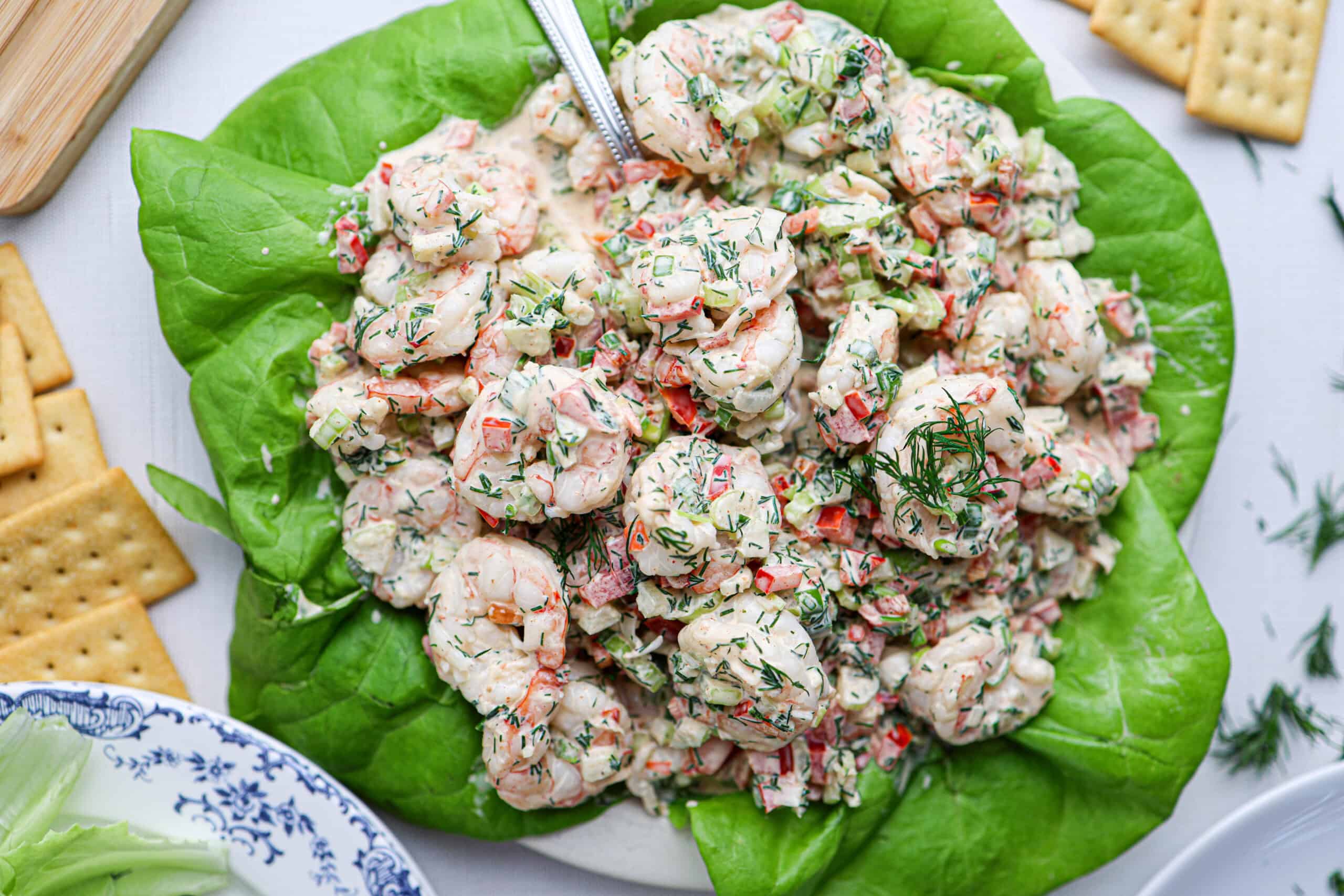A plate of creamy shrimp salad, mixed with diced vegetables and herbs, is served on a bed of lettuce, with crackers on the side.