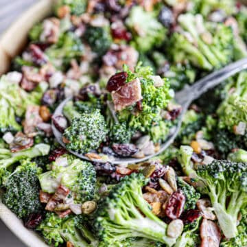 A delicious bowl of broccoli bacon salad with dried cranberries, sunflower seeds, and a creamy dressing, served with a spoon.