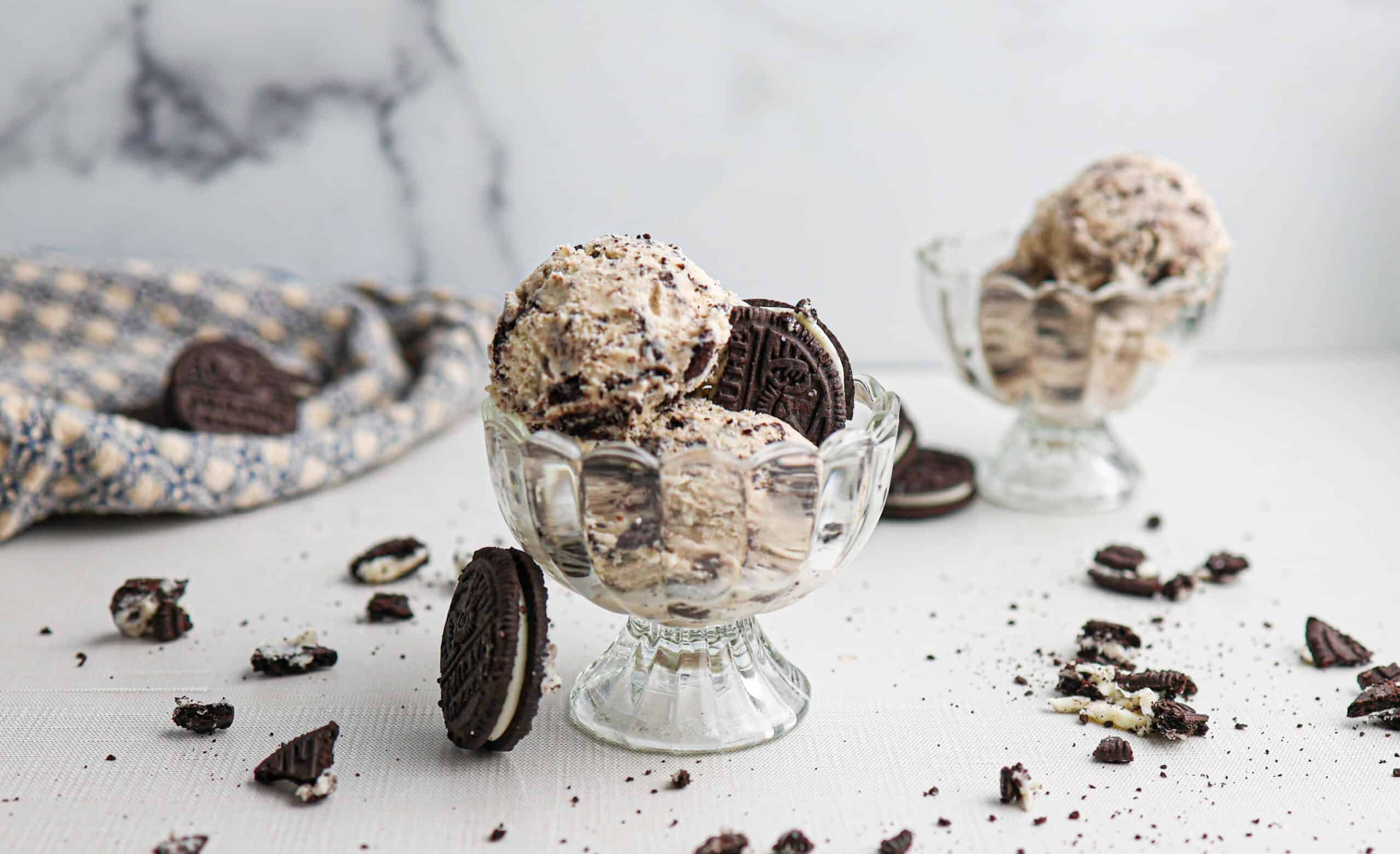 Two glass dishes filled with rich cookies and cream ice cream, generously topped with chocolate sandwich cookies, with cookie crumbs scattered on the surface for an extra touch of sweetness.